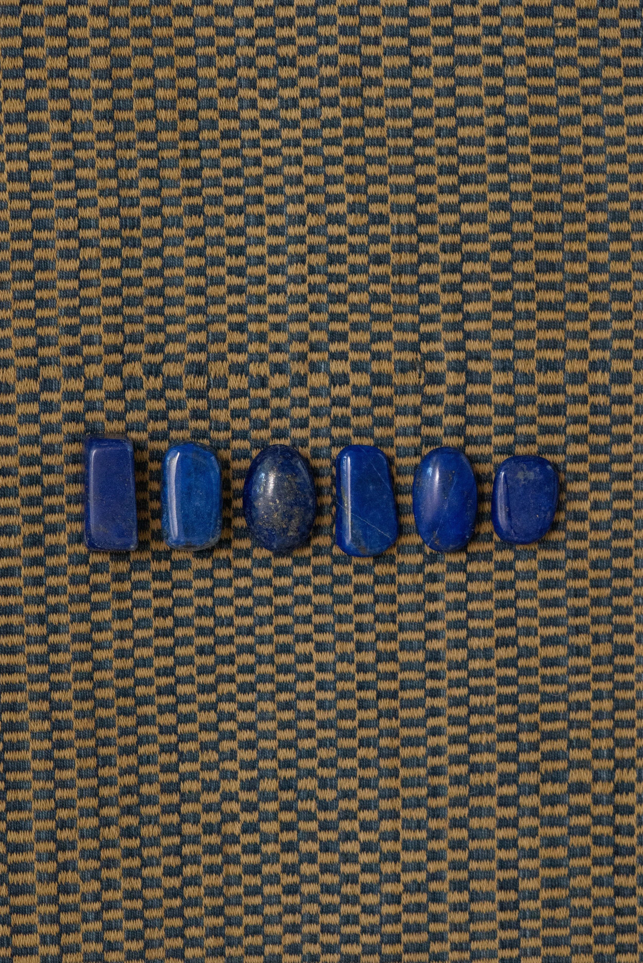 Natural lapis lazuli stones from Afghanistan, varying in shape and deep blue tones, displayed on a woven textile background.