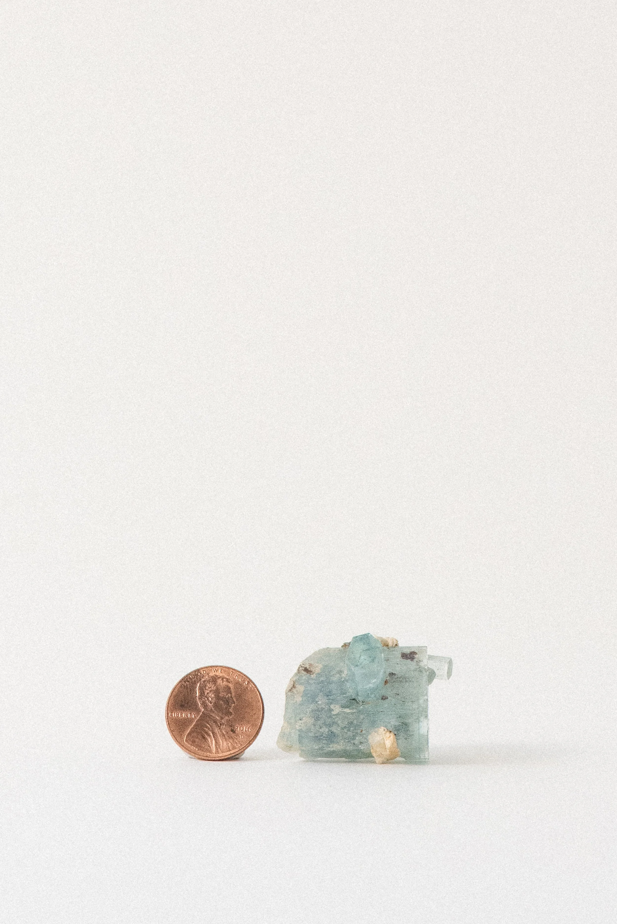 Aquamarine crystal from Erongo Mountain, Namibia, next to a penny for size reference on white background