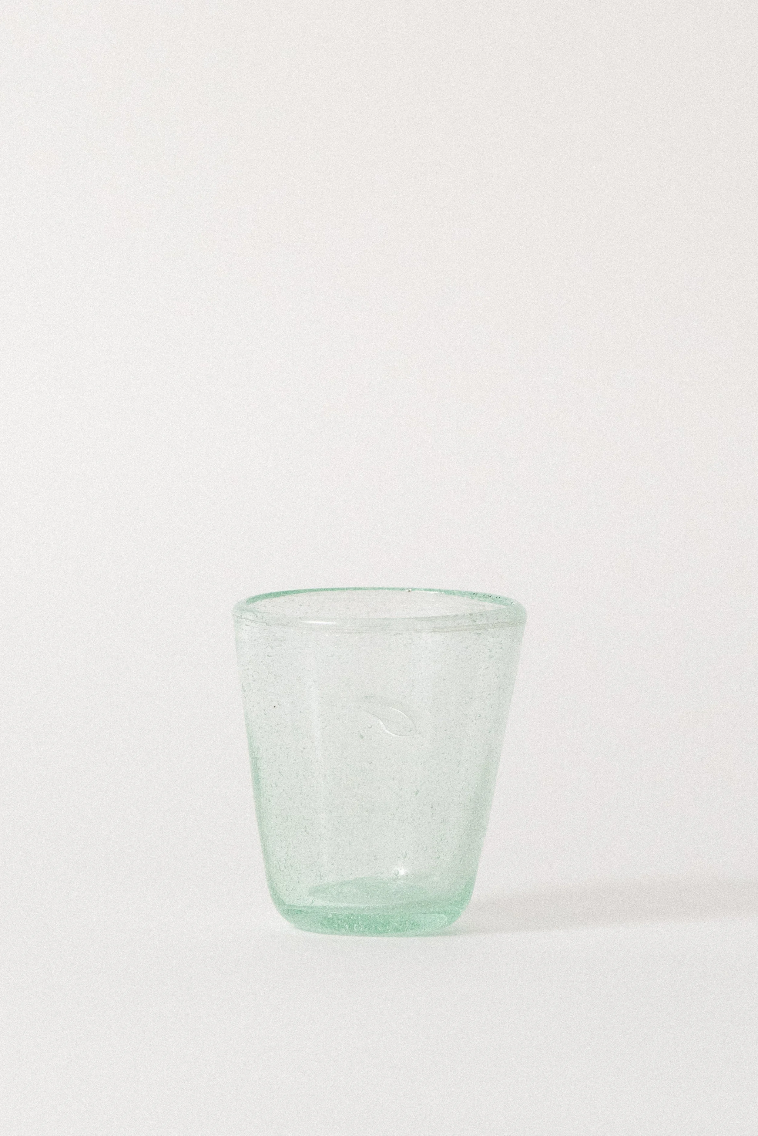 Handblown Egyptian seed glass cup with organic shape and blue-green tint, front view.