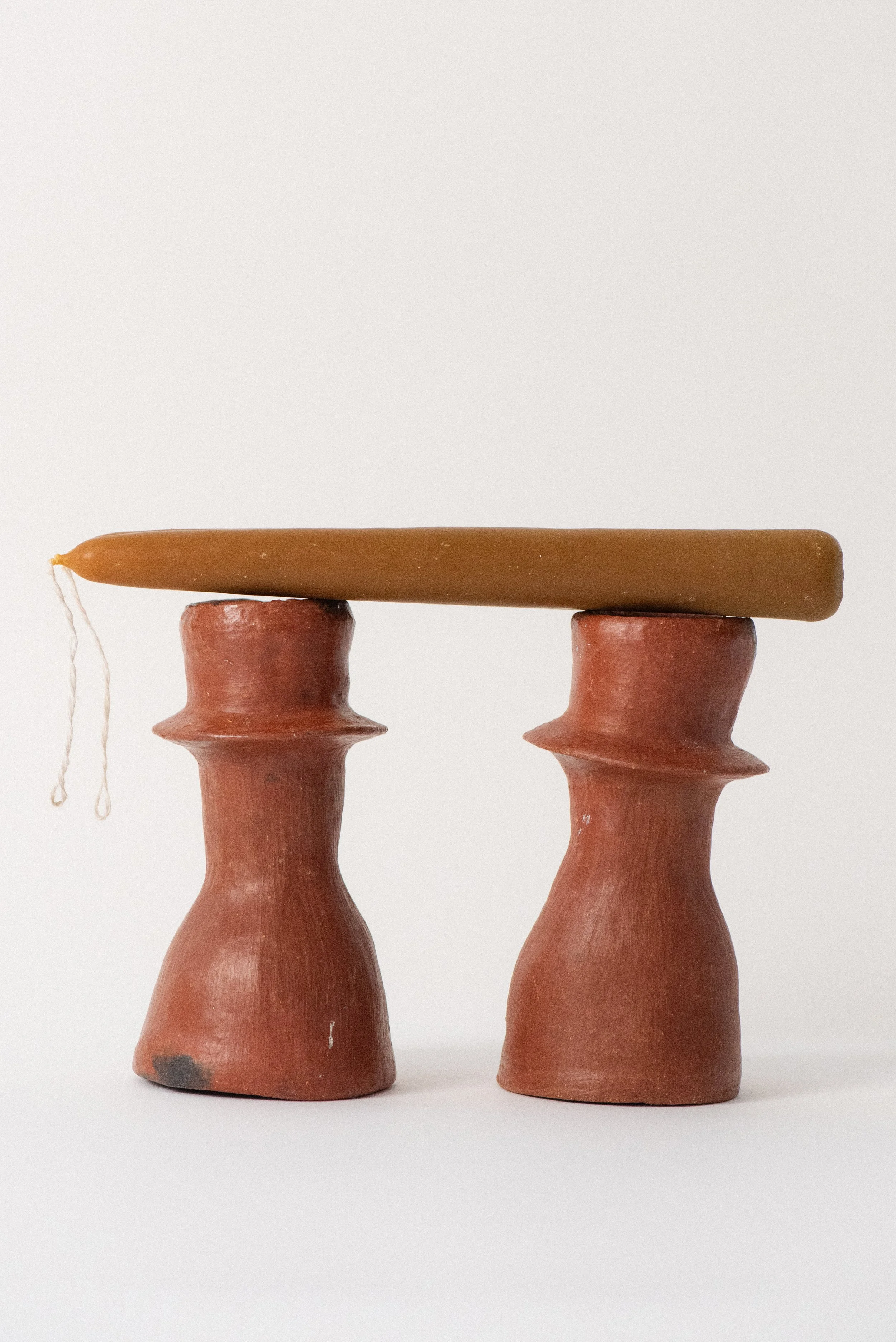 axacan red clay candle holders with a single beeswax taper candle balanced horizontally on top.