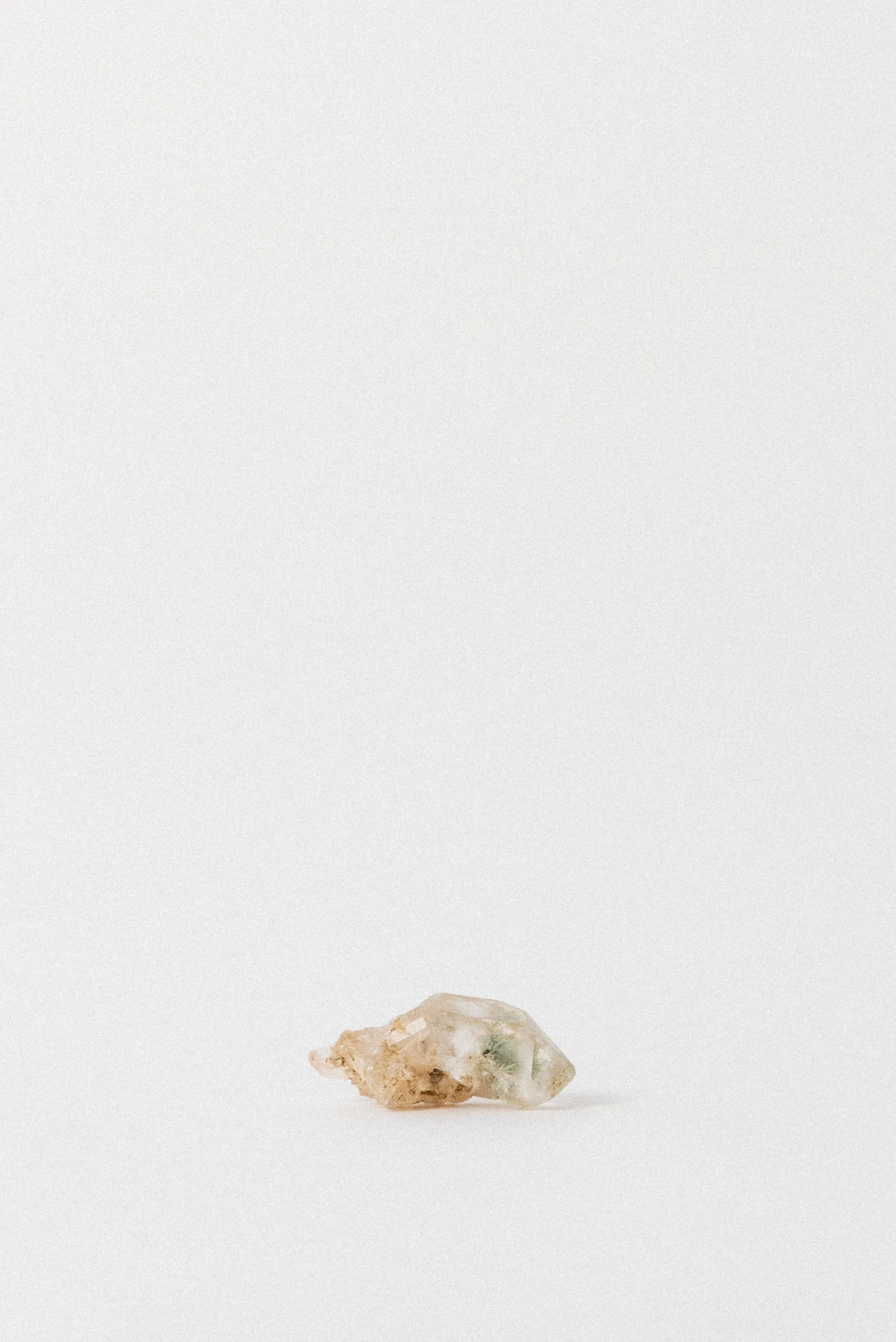 Small clear quartz point with green pumpellyite inclusions from Andhra Pradesh, India, photographed on a white background.