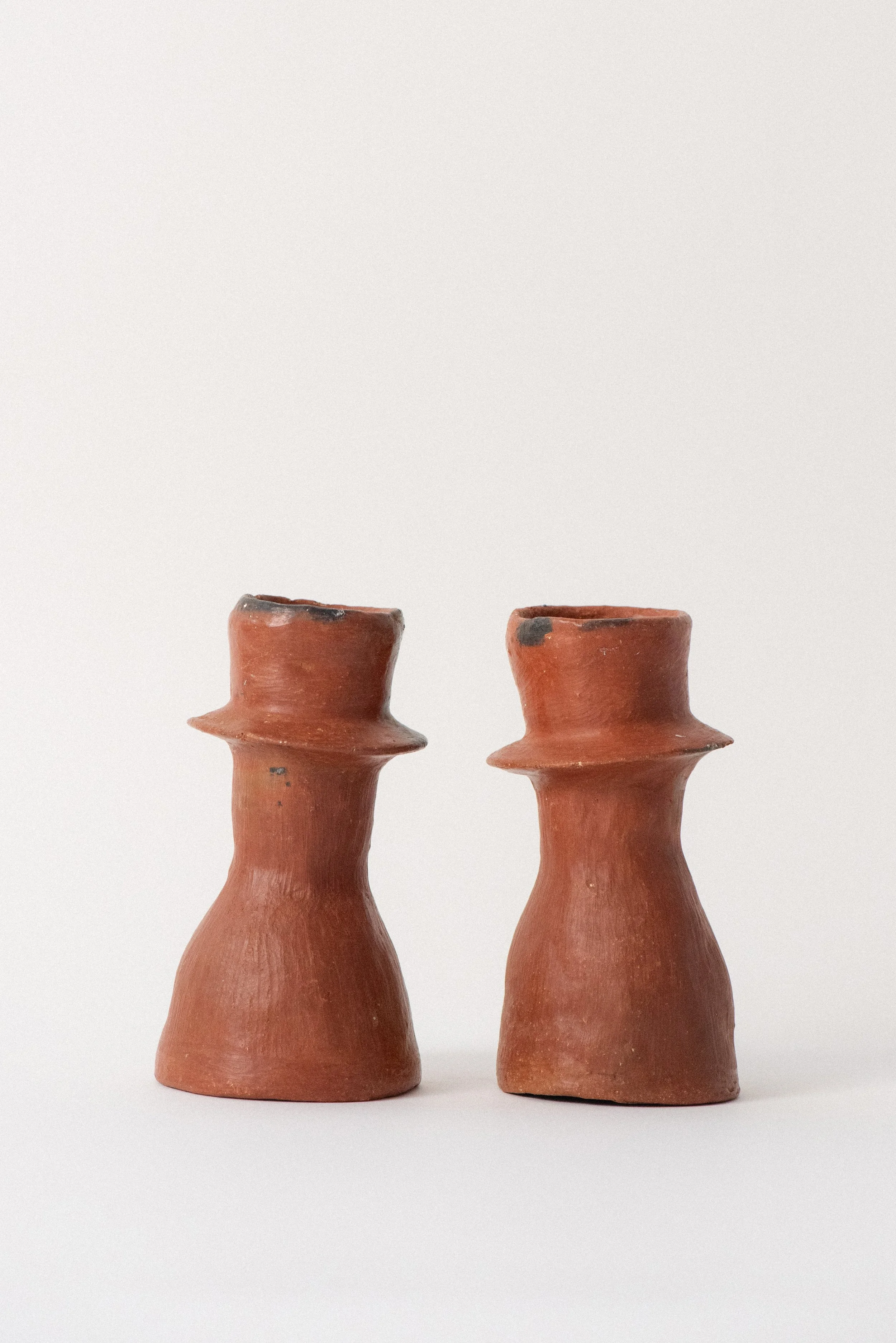 Side view of a pair of rustic handmade red clay candle holders from Oaxaca.