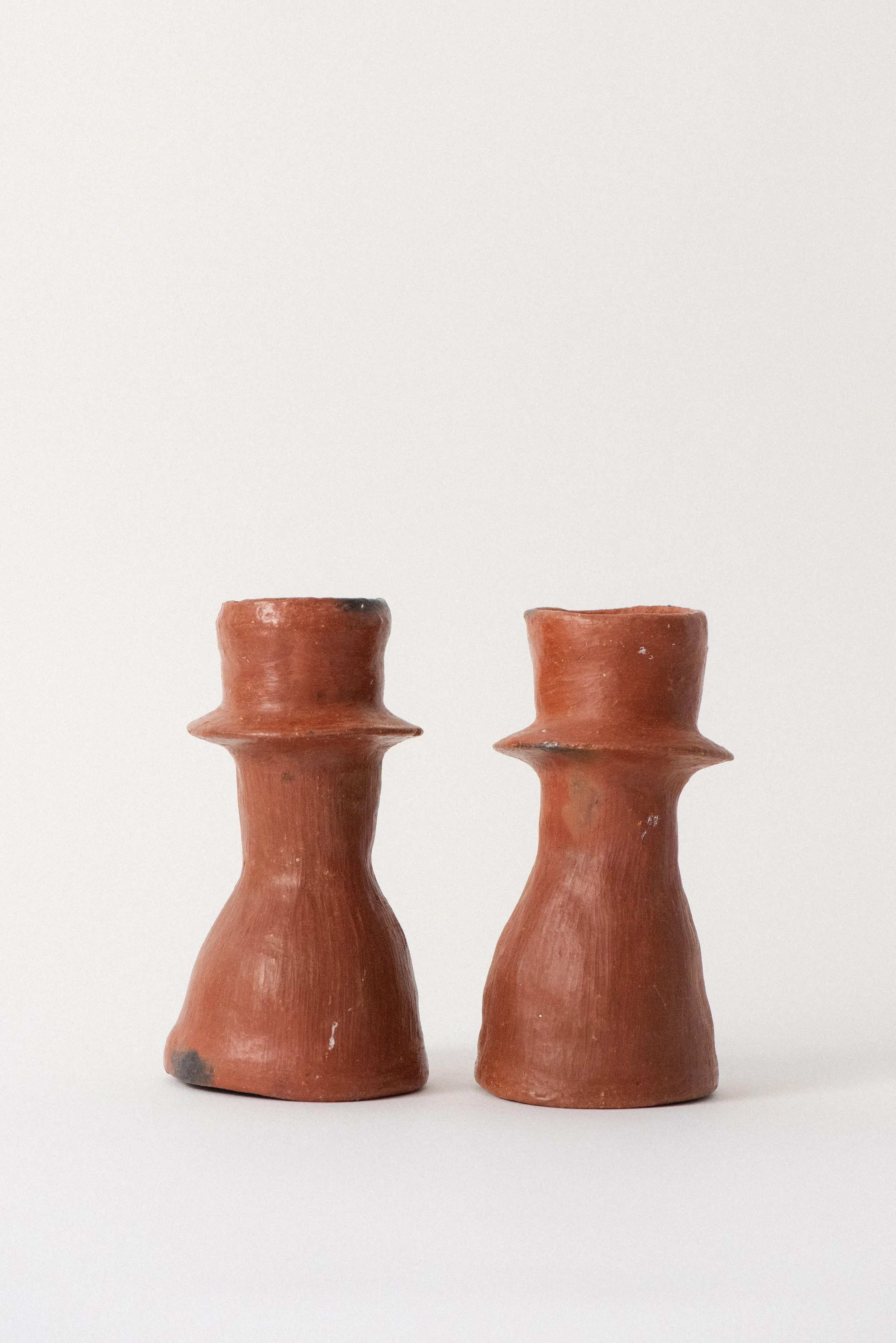 Alternate side view of two handcrafted red clay candle holders from Oaxaca, showcasing their organic shape.