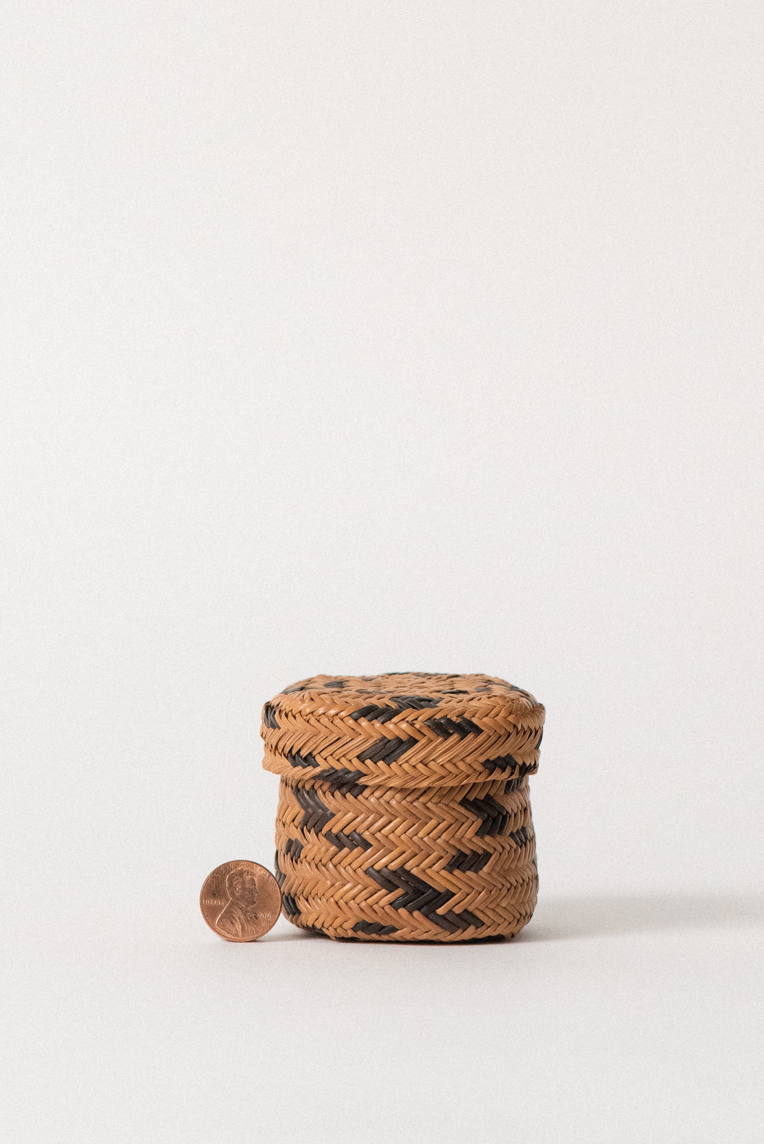 Miniature handwoven Tarahumara basket from 1960s Mexico made of pine needles, shown with penny for scale.