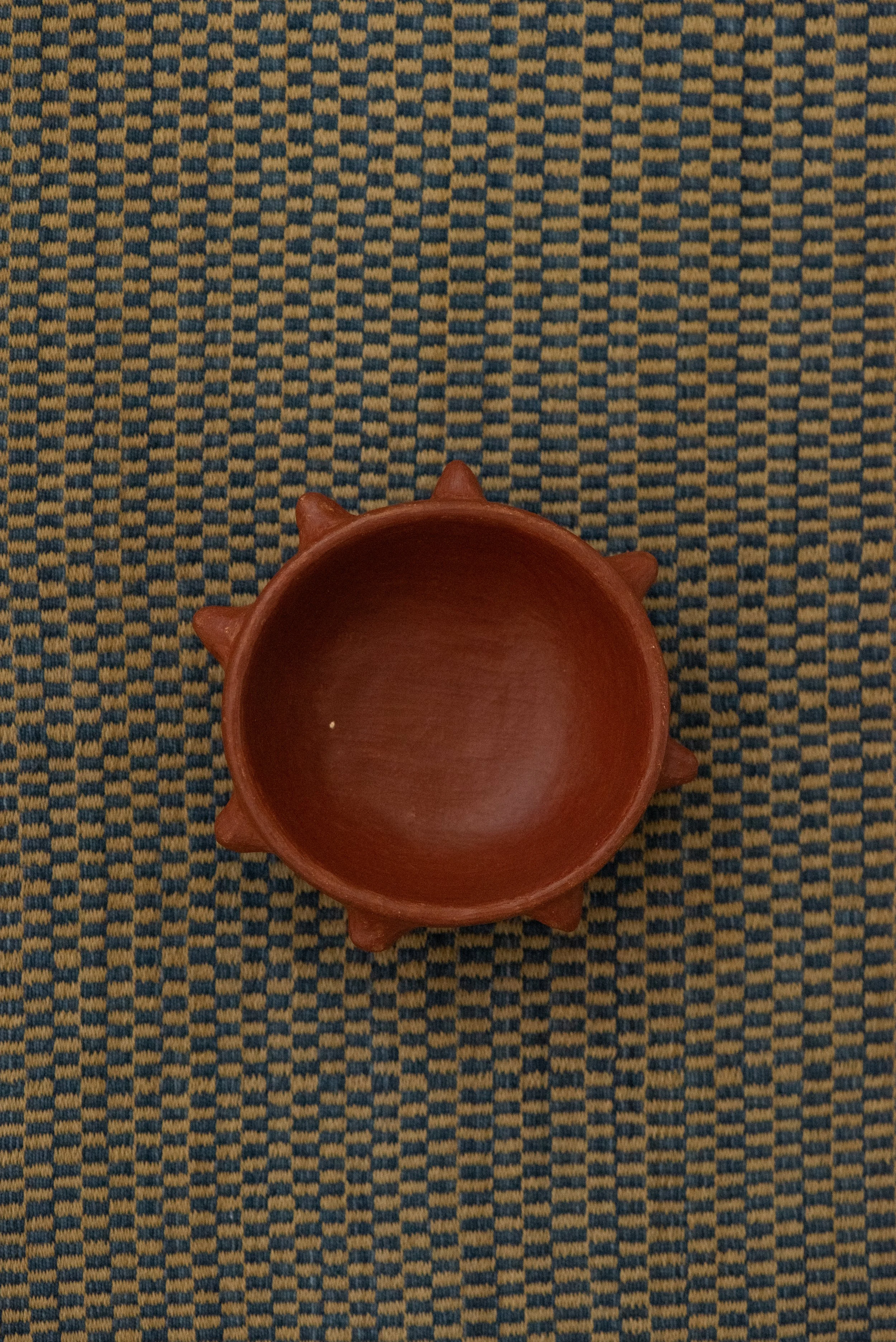 Barro Rojo red clay spiked bowl from Oaxaca, handmade with distinctive raised points around the rim, displayed on a woven textile background.
