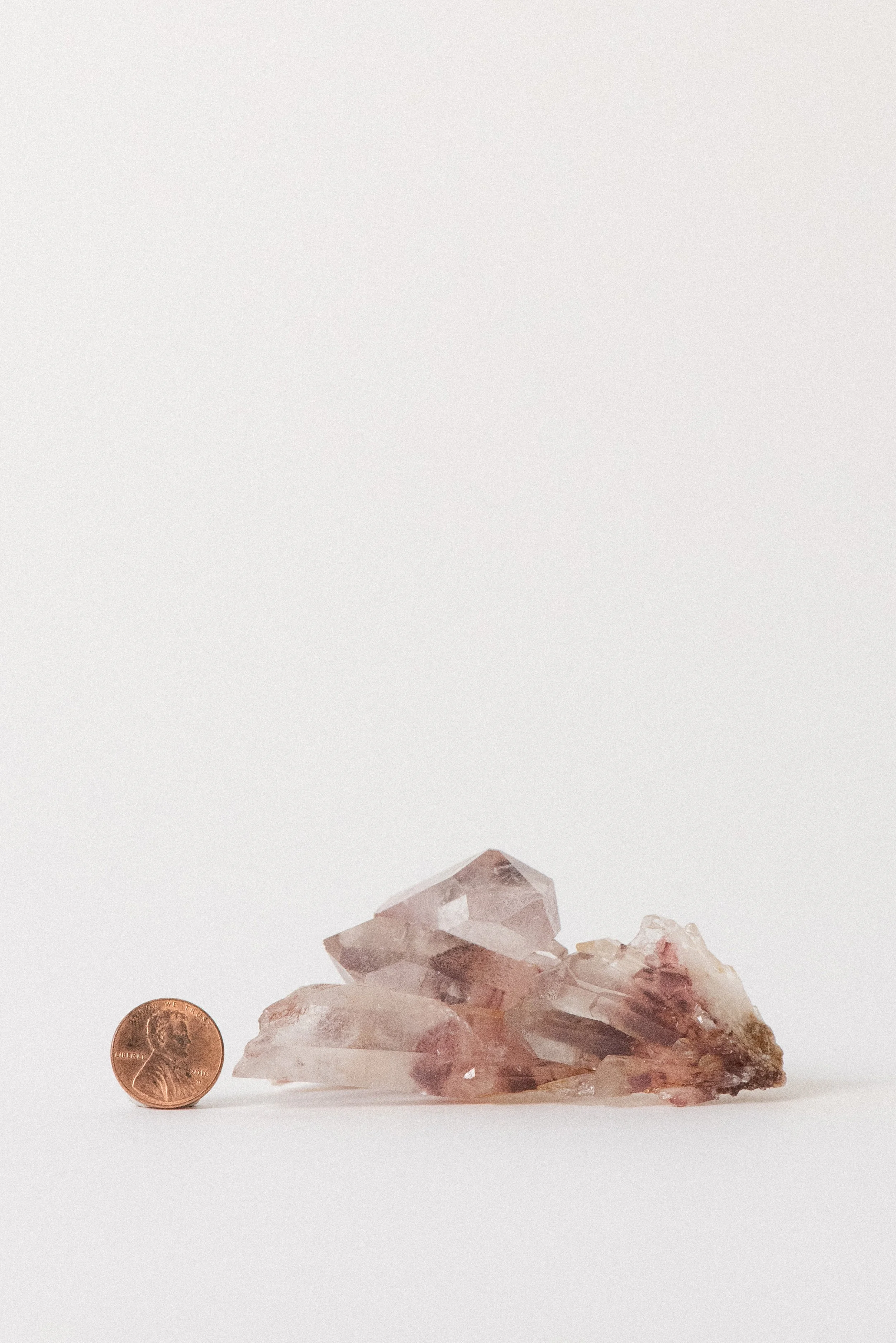 Sunset phantom quartz cluster next to a penny for size reference, showing medium-sized formation.