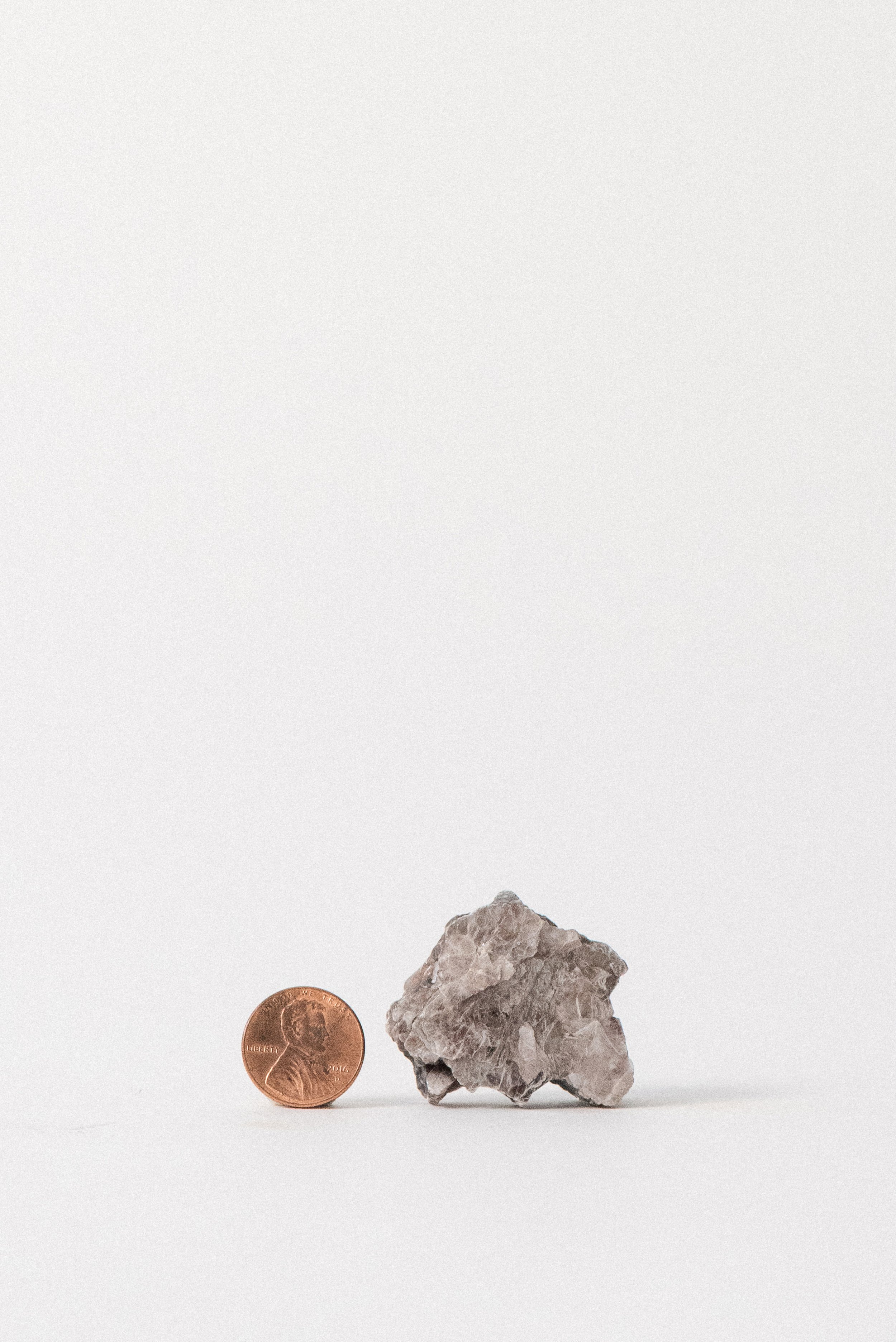 Raw muscovite mica from Taquaral, Minas Gerais, Brazil, shown next to a penny for scale. Silvery layers and earthy tone. Part of the Crystal Voyager collection.