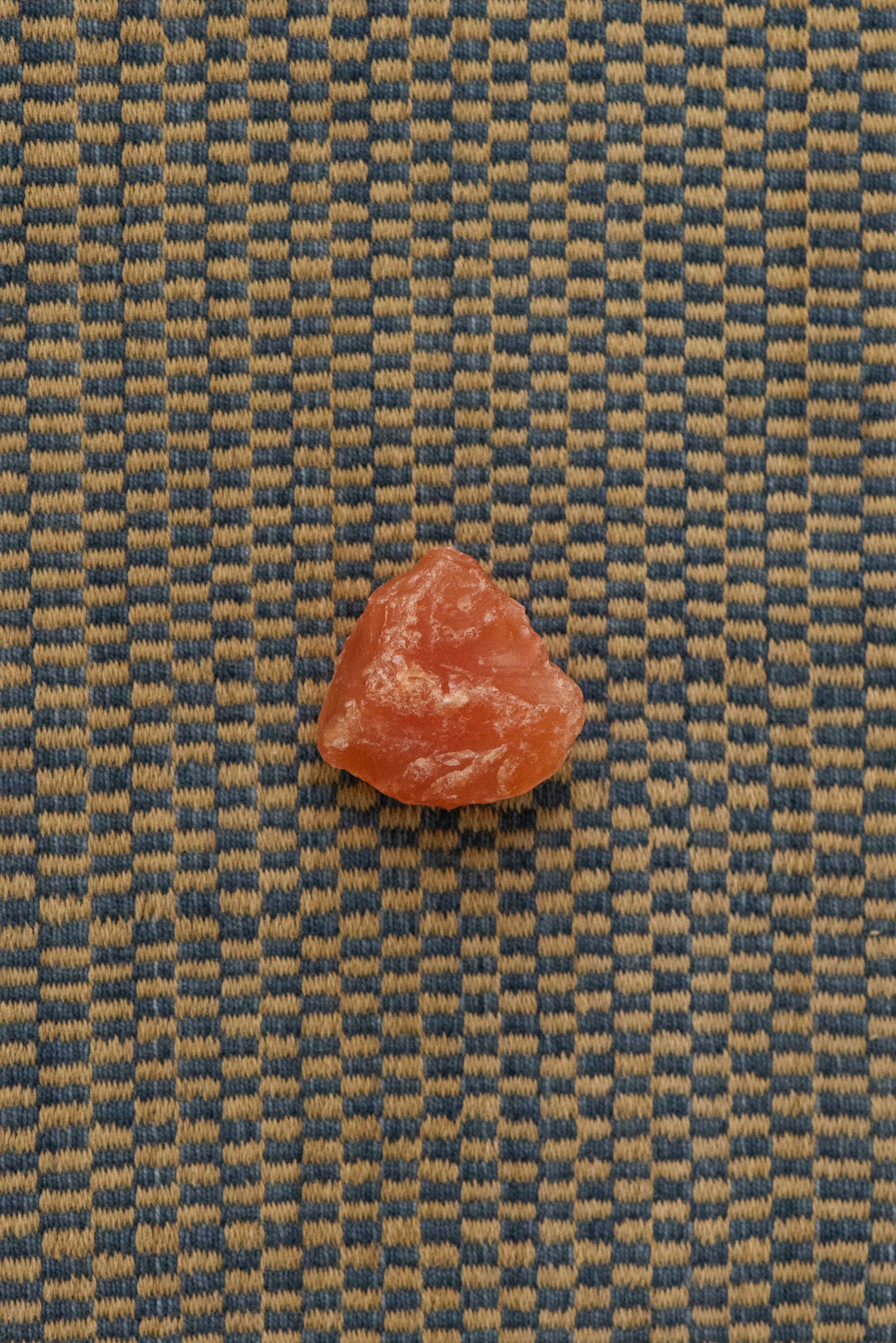 Vintage raw carnelian crystal from Africa in bright orange color, shown on patterned background