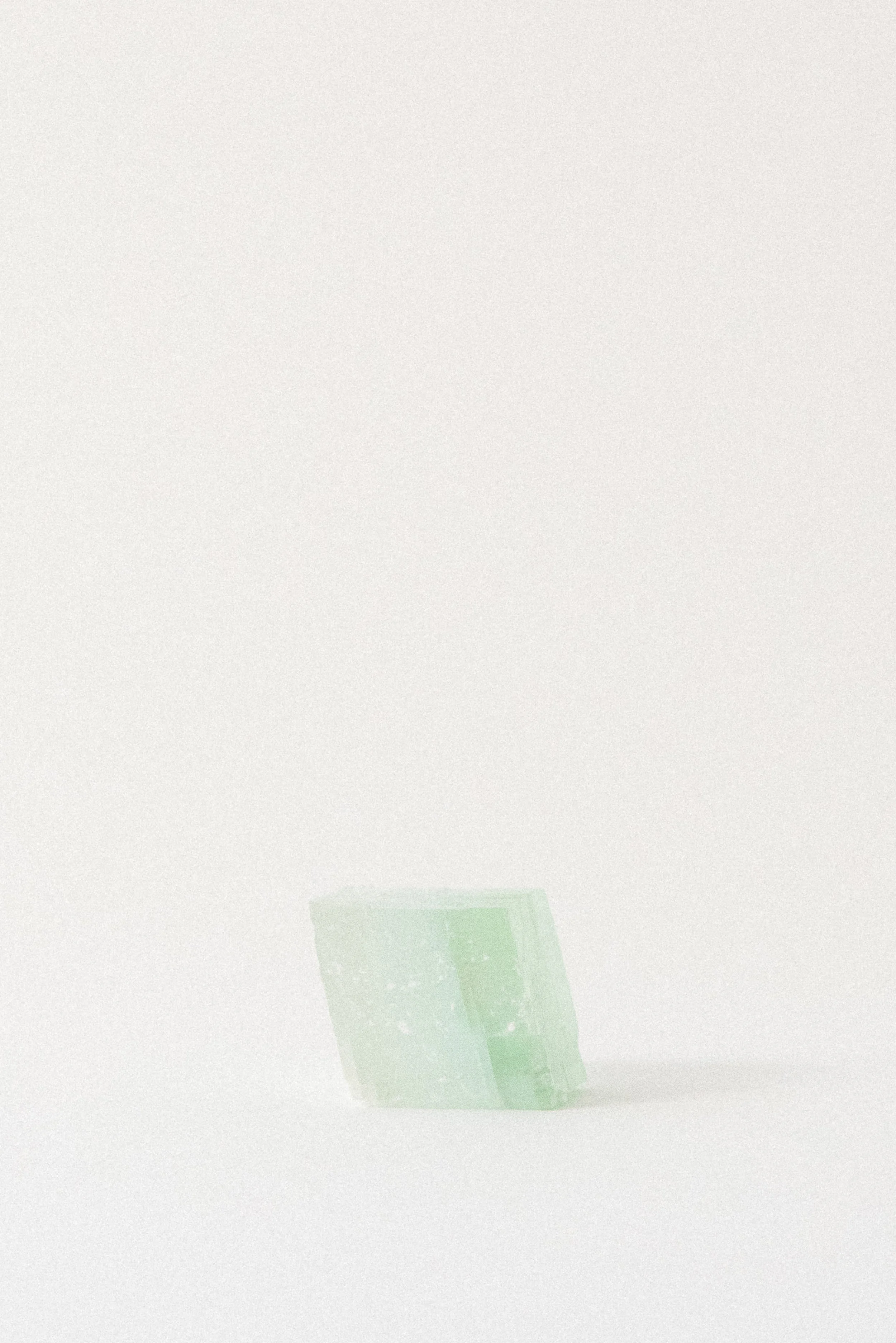Pale green calcite rhomboid crystal from Mexico resting on a soft white surface, with diffuse natural light and gentle shadowing