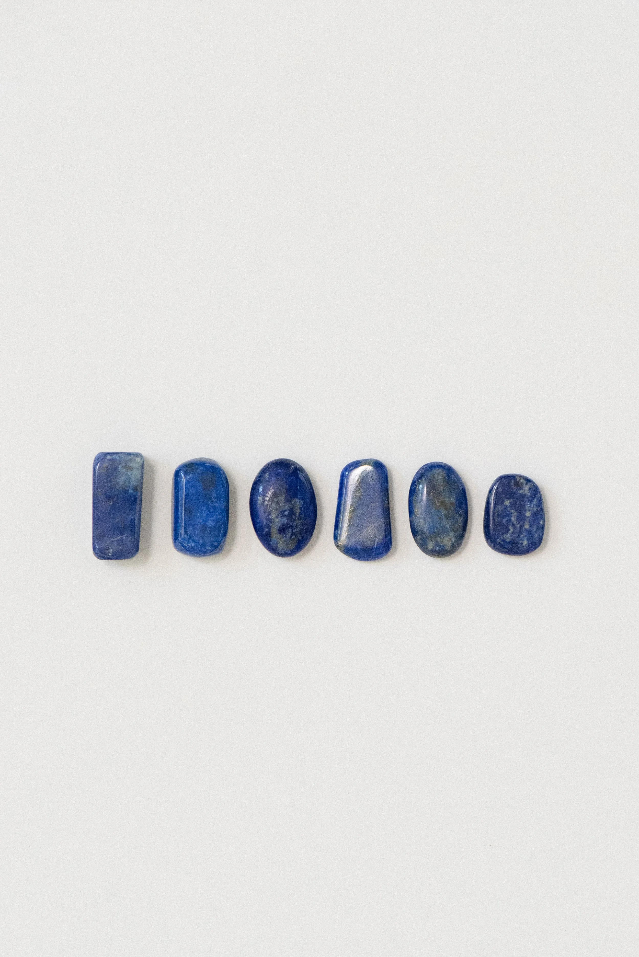 Six natural lapis lazuli polished stones from Afghanistan displayed on a white background, showcasing variations in shape and color.