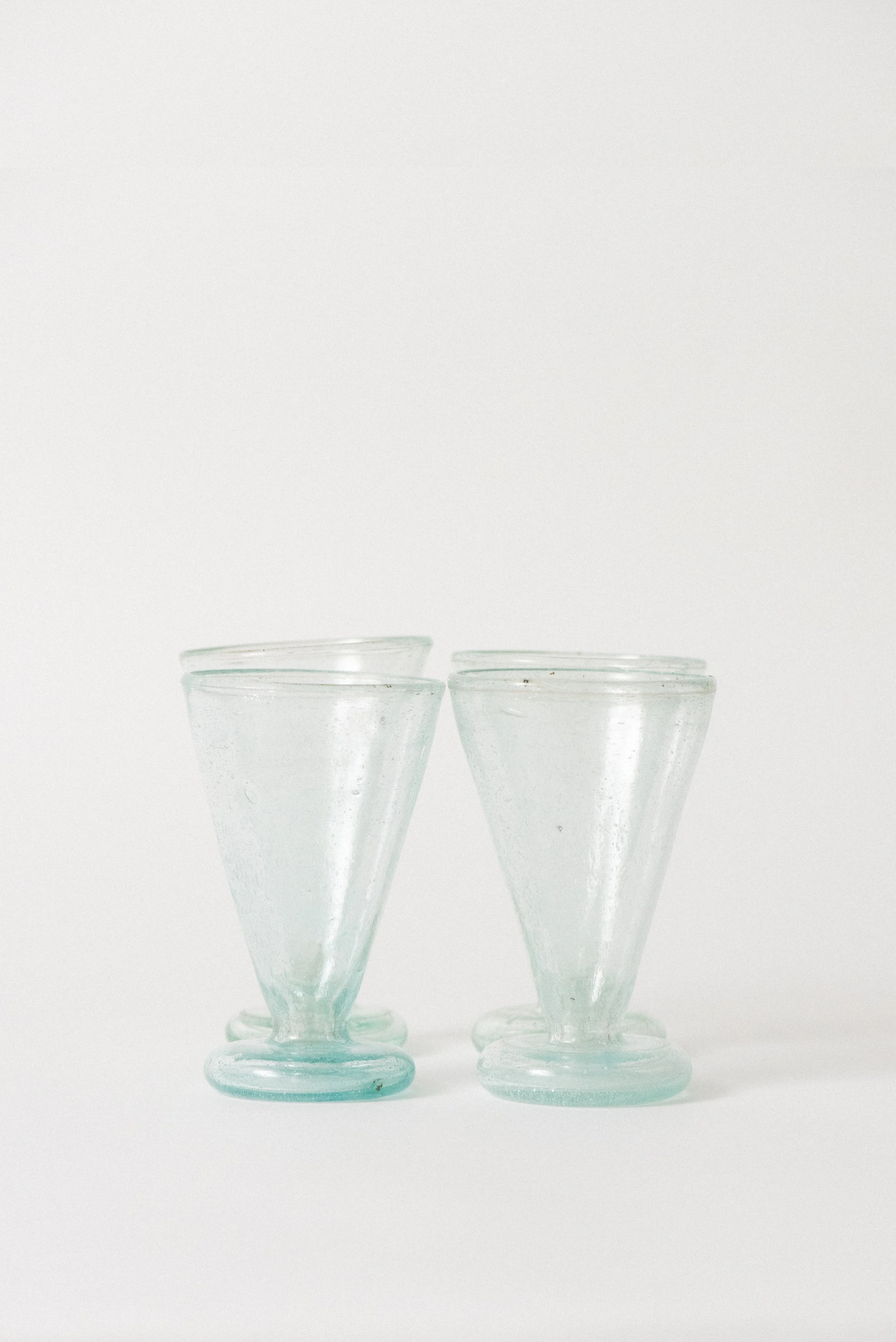 Front view of four handblown Egyptian tea glasses with wide rims, rounded footed bases, and light blue seed glass bubbles.