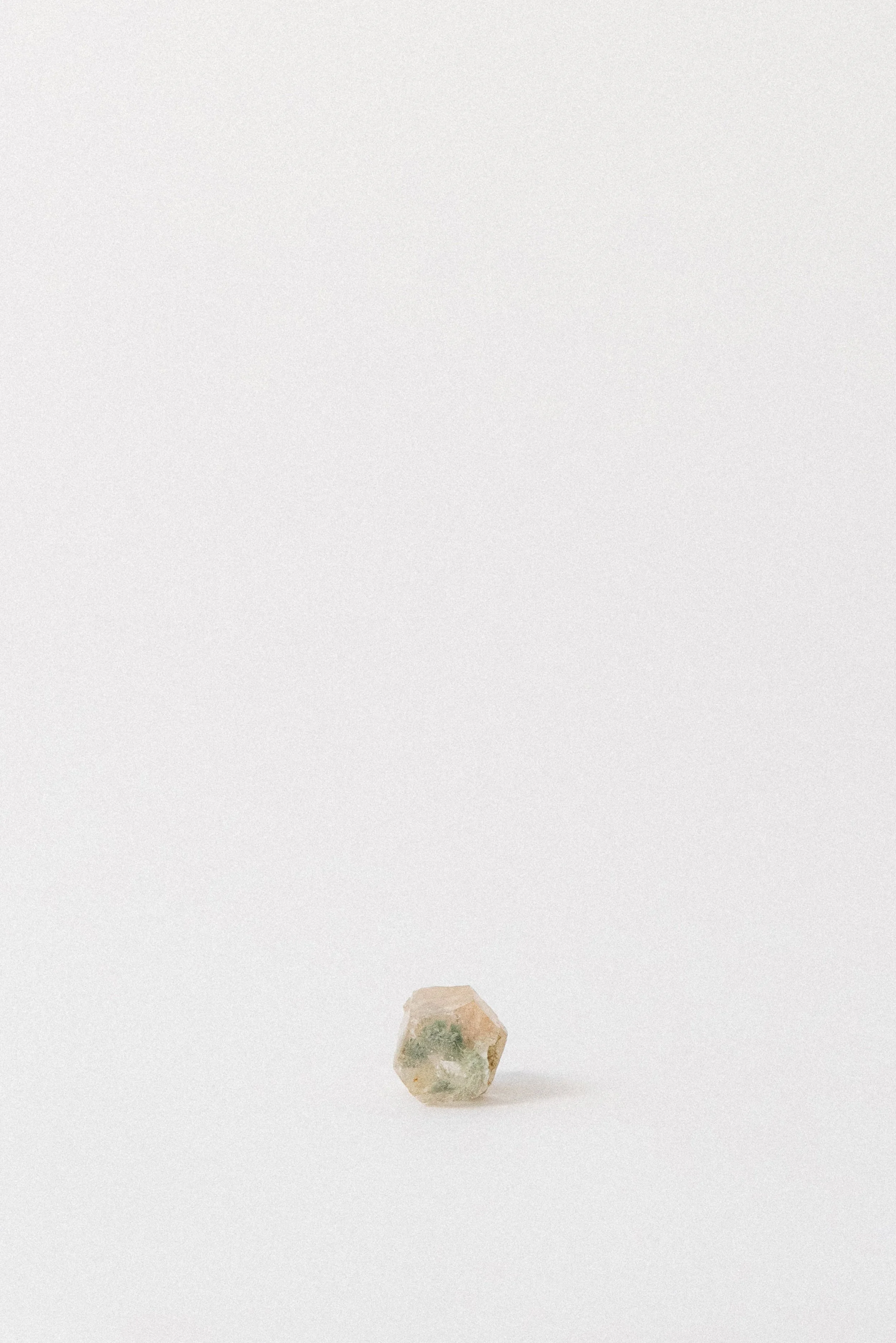 Small clear quartz crystal with green pumpellyite inclusion from Andhra Pradesh, India, standing upright on a white background.