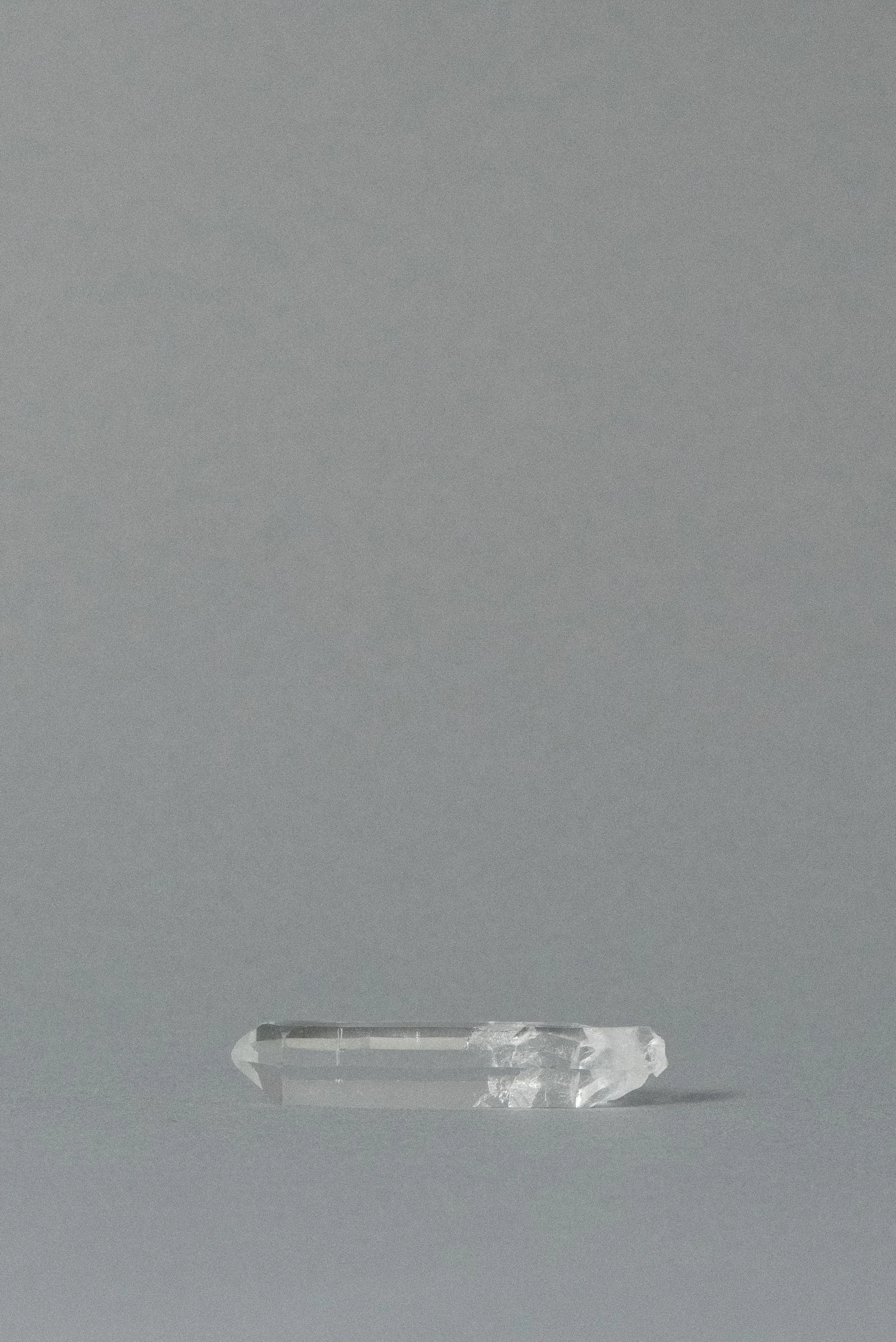 Single-terminated clear quartz point crystal from Brazil photographed on a soft gray background.
