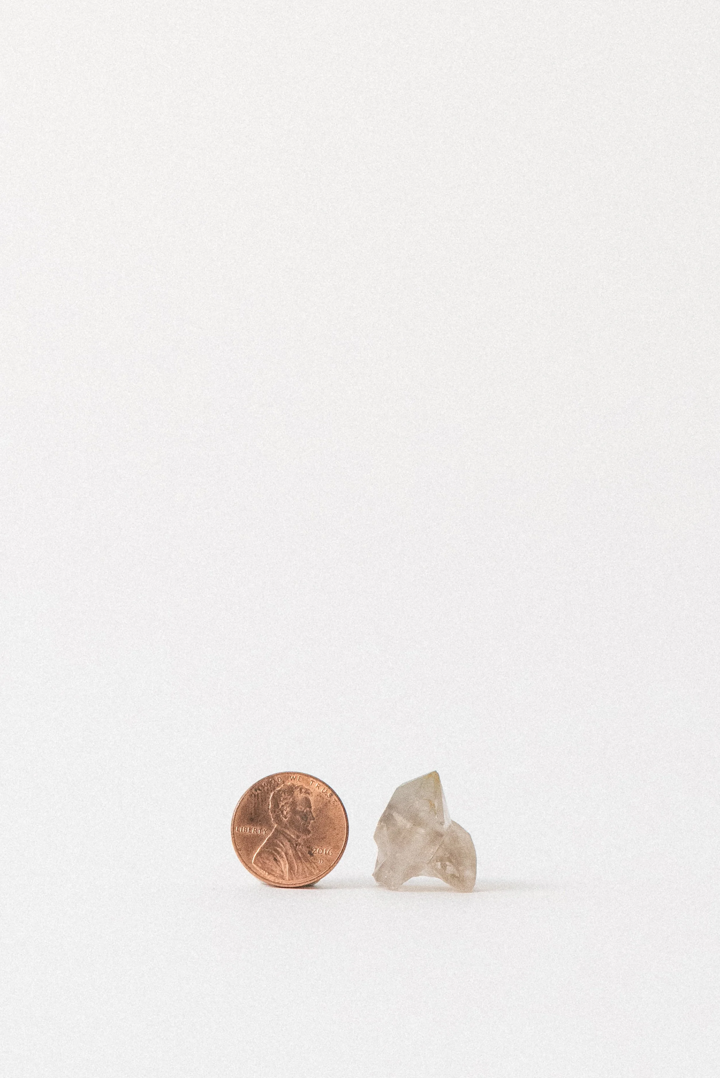 Small smoky quartz cluster from Erongo Mountain, Namibia, shown next to a penny for scale. Features translucent crystal points with a light smoky hue.