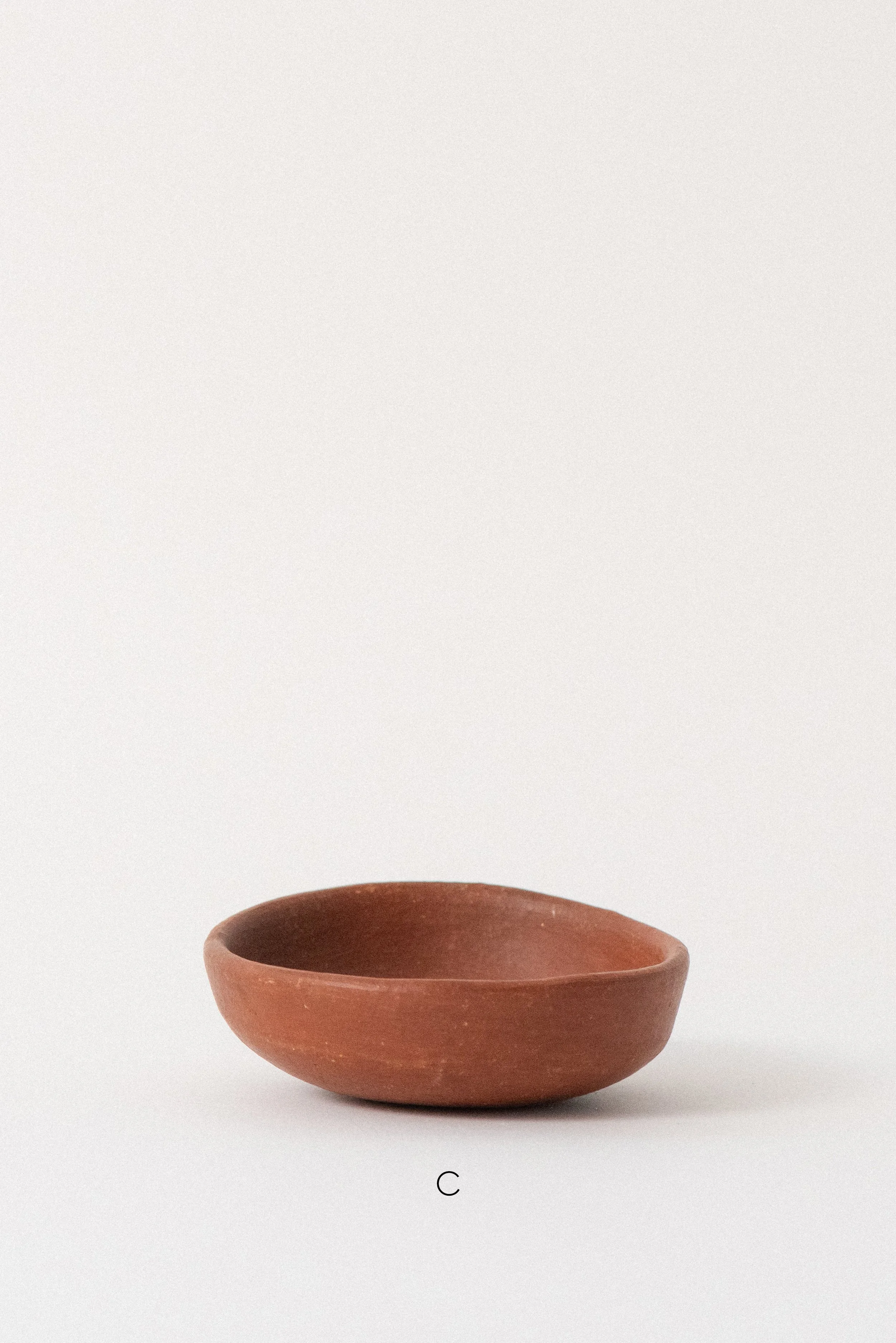 Single handmade barro rojo red clay bowl labeled C, crafted in Oaxaca, Mexico, displayed against a white background — rustic and versatile kitchenware.