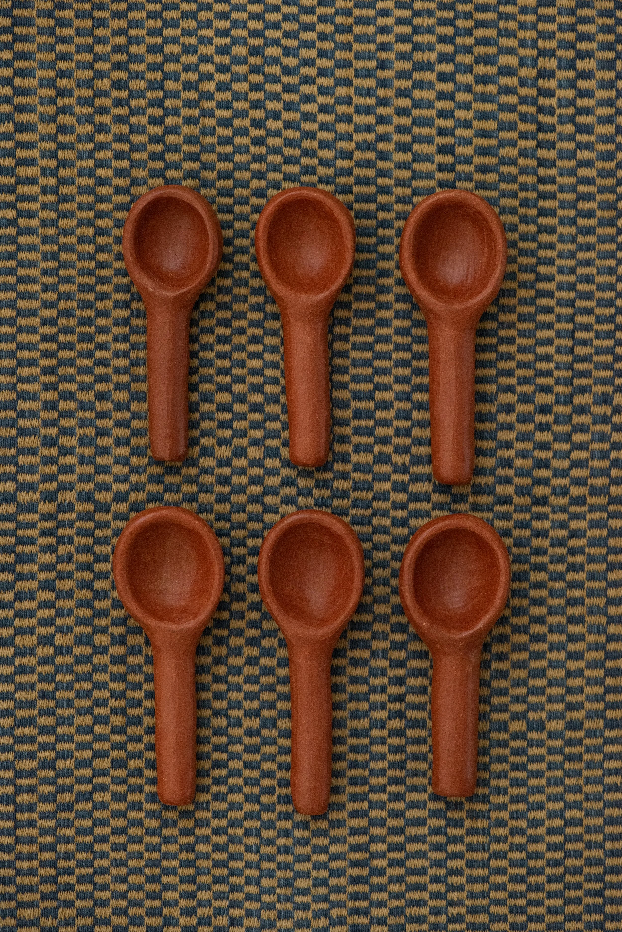 Set of six handmade Barro Rojo red clay spoons from Oaxaca, displayed on a woven textile background.
