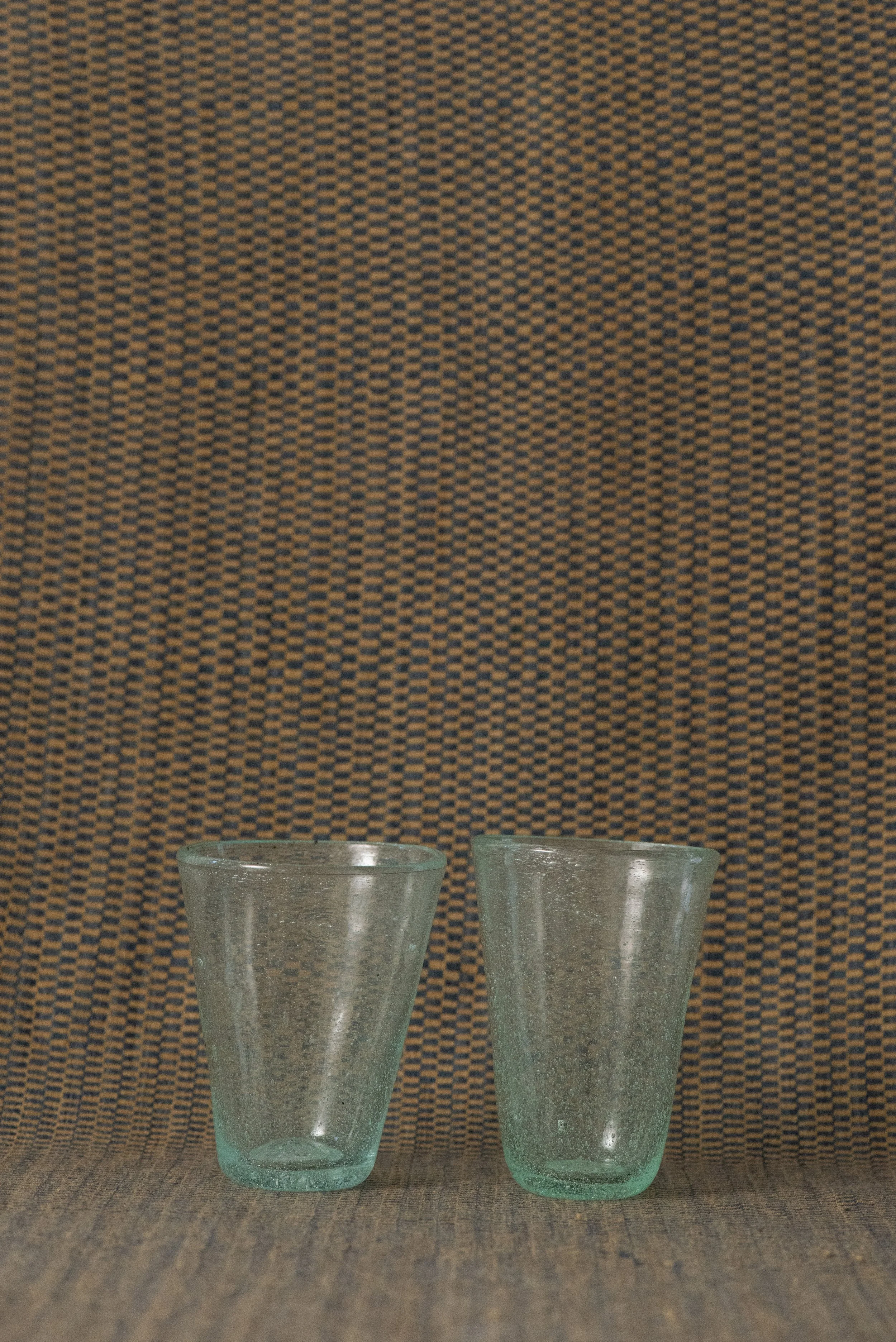 Pair of handblown Egyptian seed glass tumblers in light green with natural air bubbles, displayed on a woven textile background.