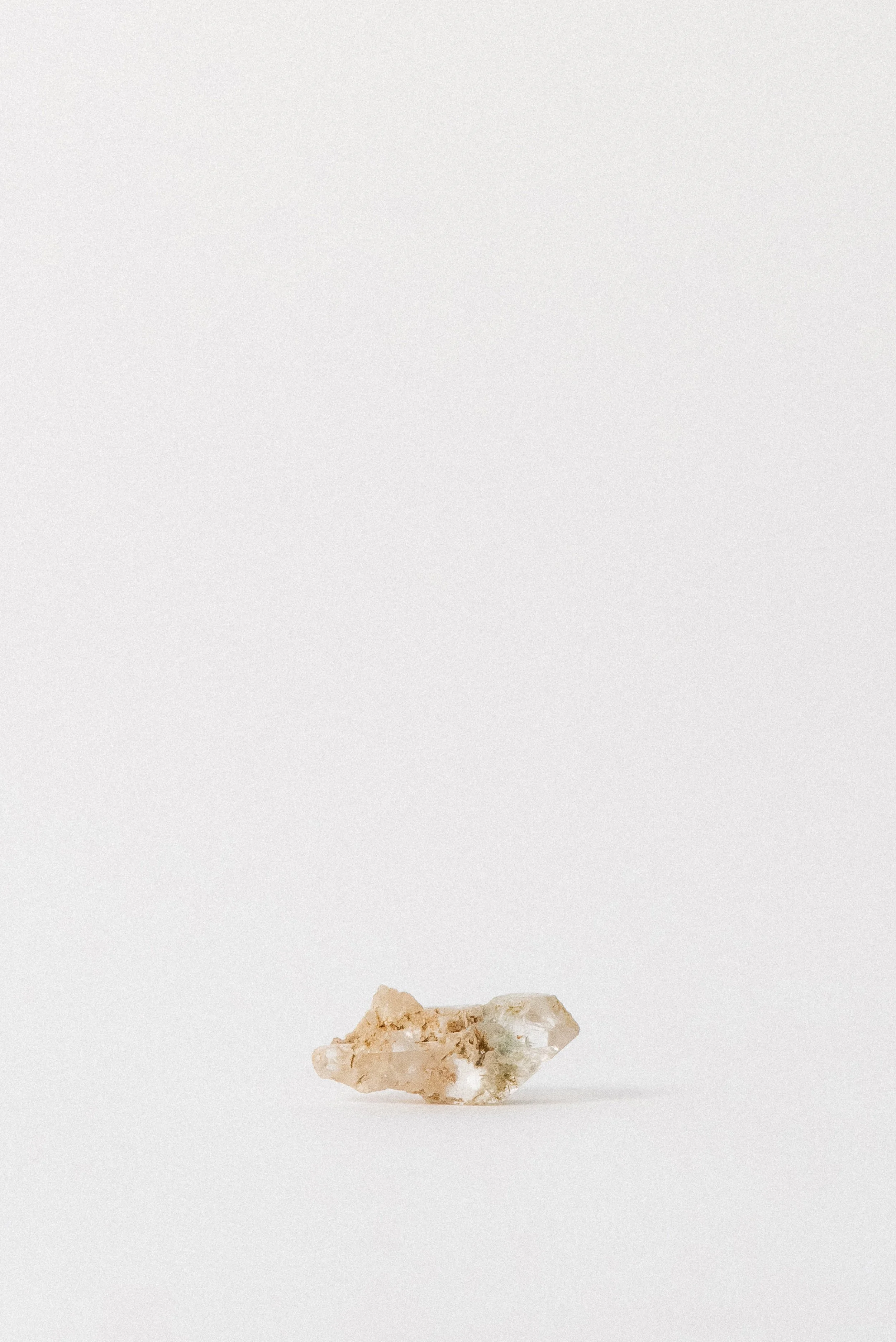 Clear quartz crystal with green pumpellyite inclusion and earthy matrix from Andhra Pradesh, India, shown on a clean white background.