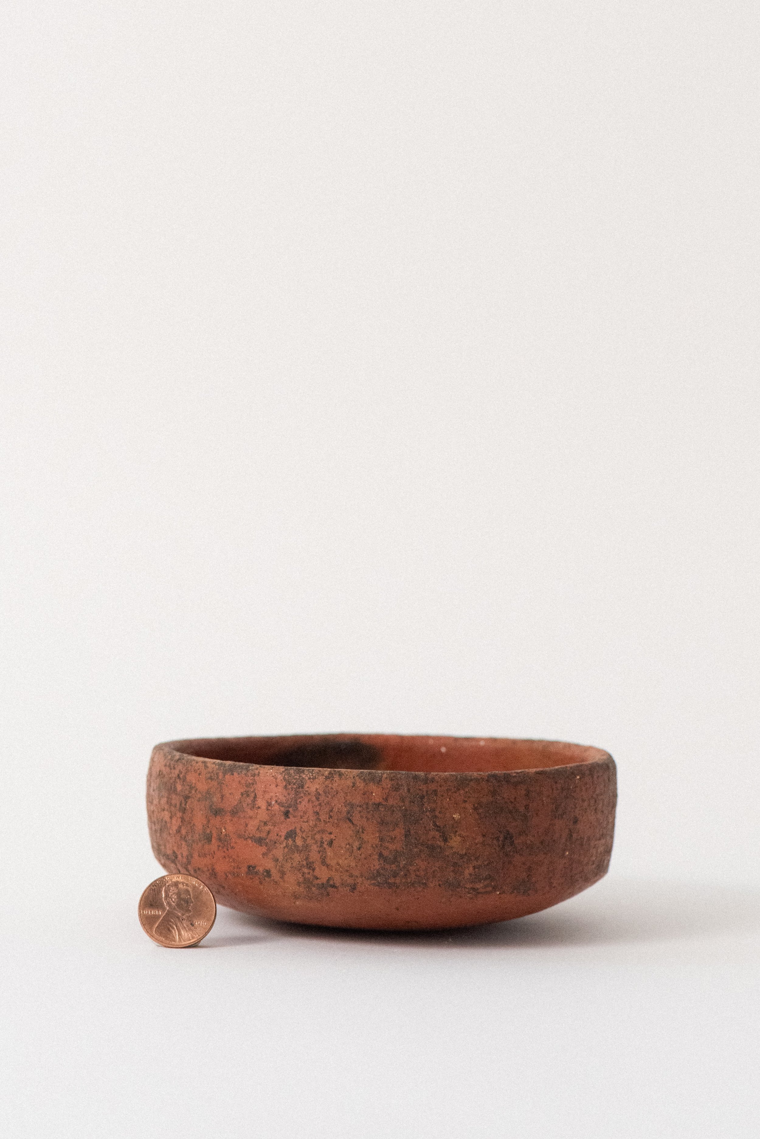Rustic Oaxacan red clay pottery bowl with penny for size reference on white background