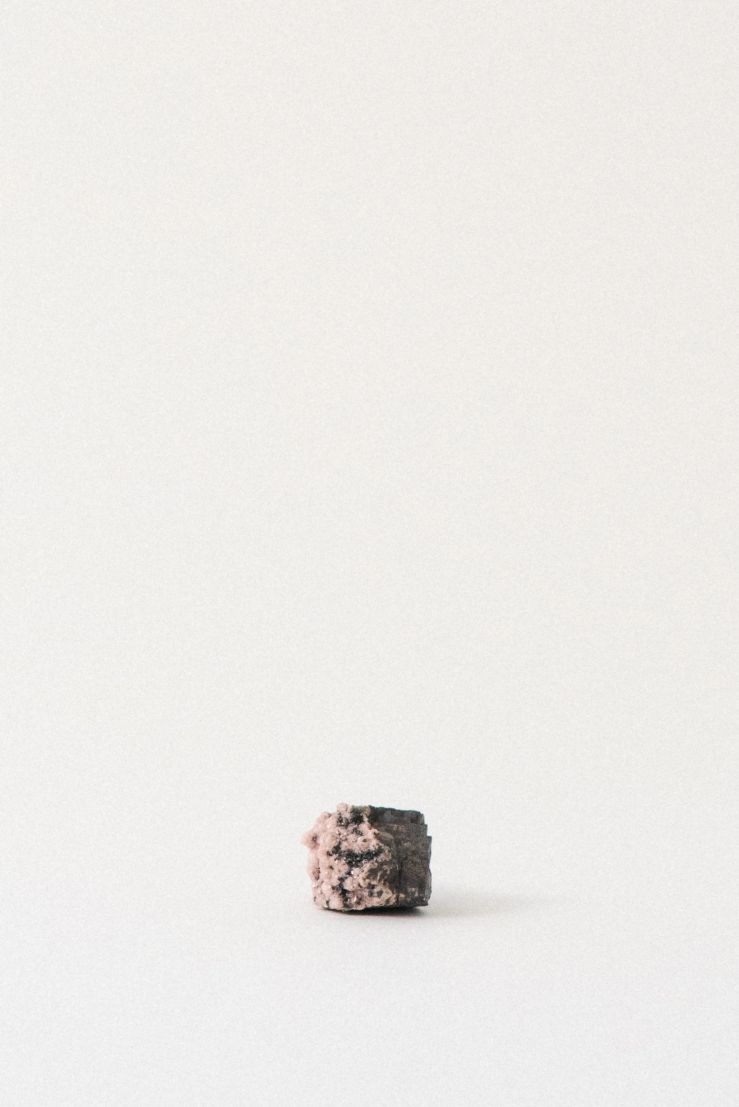 Rhodochrosite crystal with soft pink formations on a dark manganese-rich matrix, from N’Chwaning Mine, South Africa, against a minimal white backdrop.