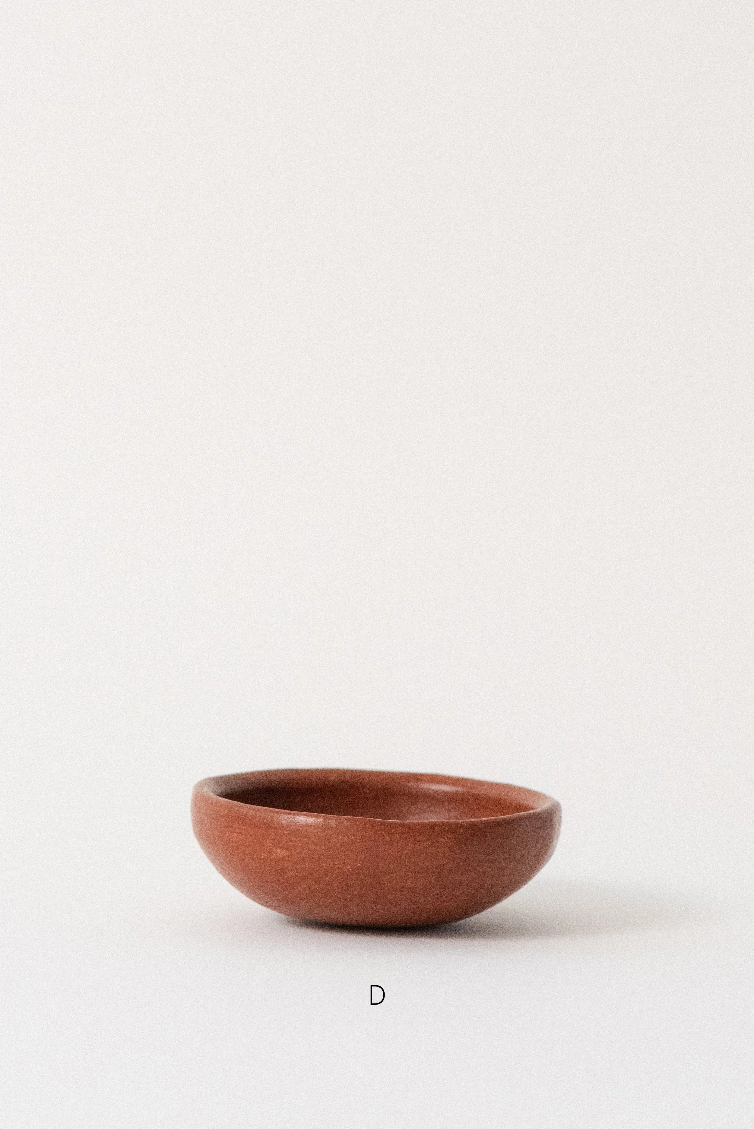 Single handmade barro rojo red clay bowl labeled D, crafted in Oaxaca, Mexico, displayed against a white background — rustic and versatile kitchenware.