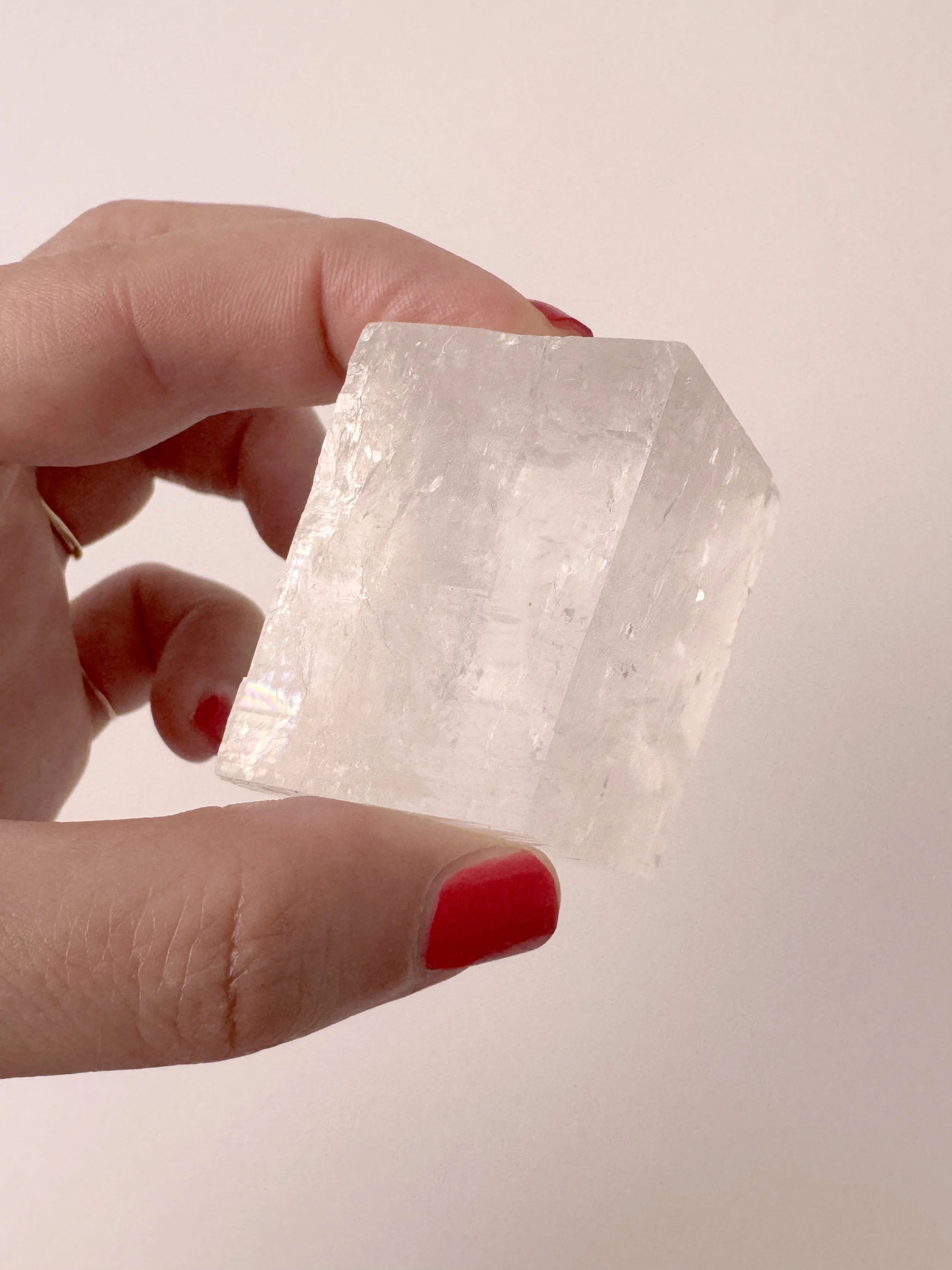 Hand holding a transparent optical calcite crystal with rhombohedral geometry. Ethically sourced from Mexico.