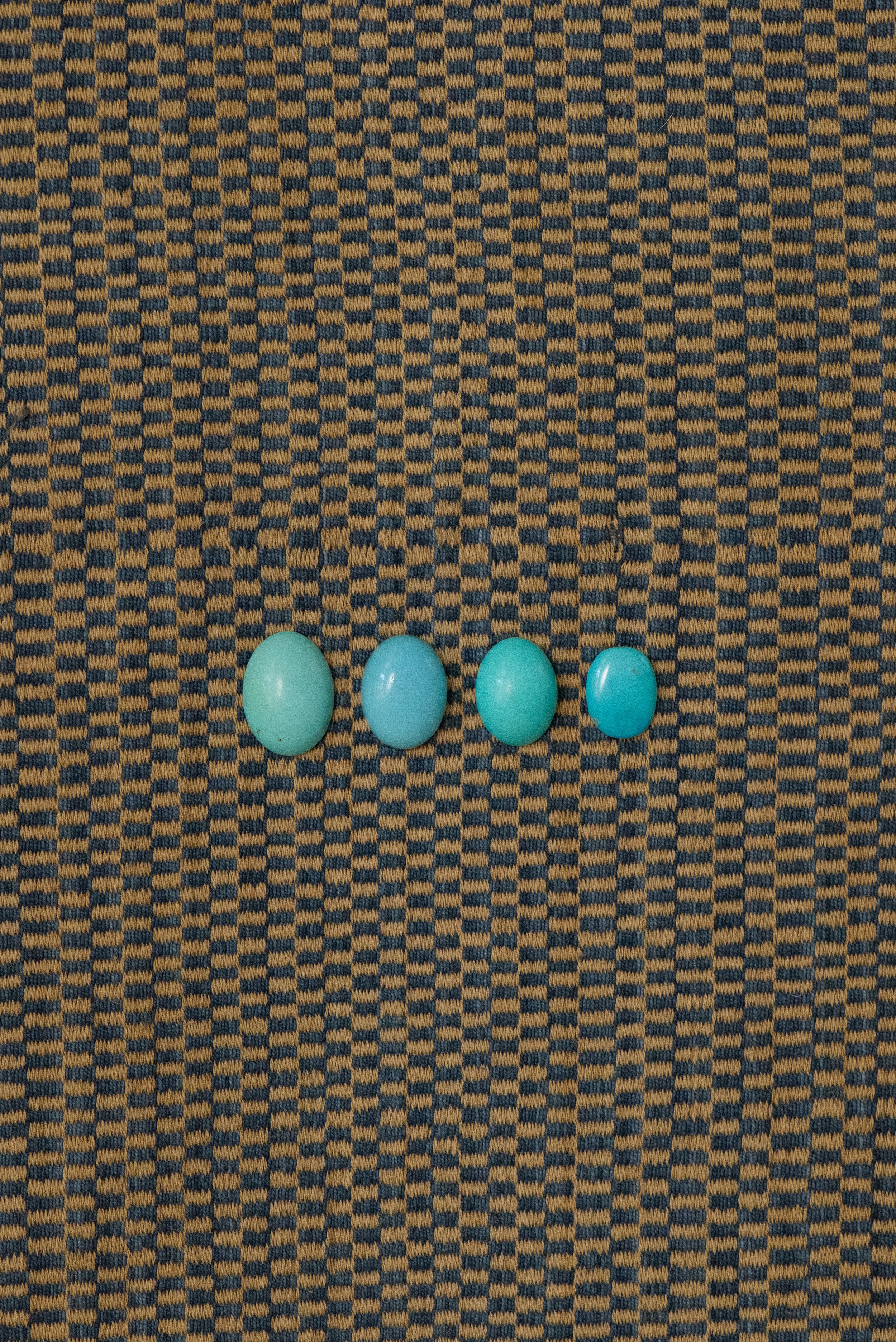 Egyptian turquoise cabochons from the Sinai region, polished and arranged in a row on a woven textile background.