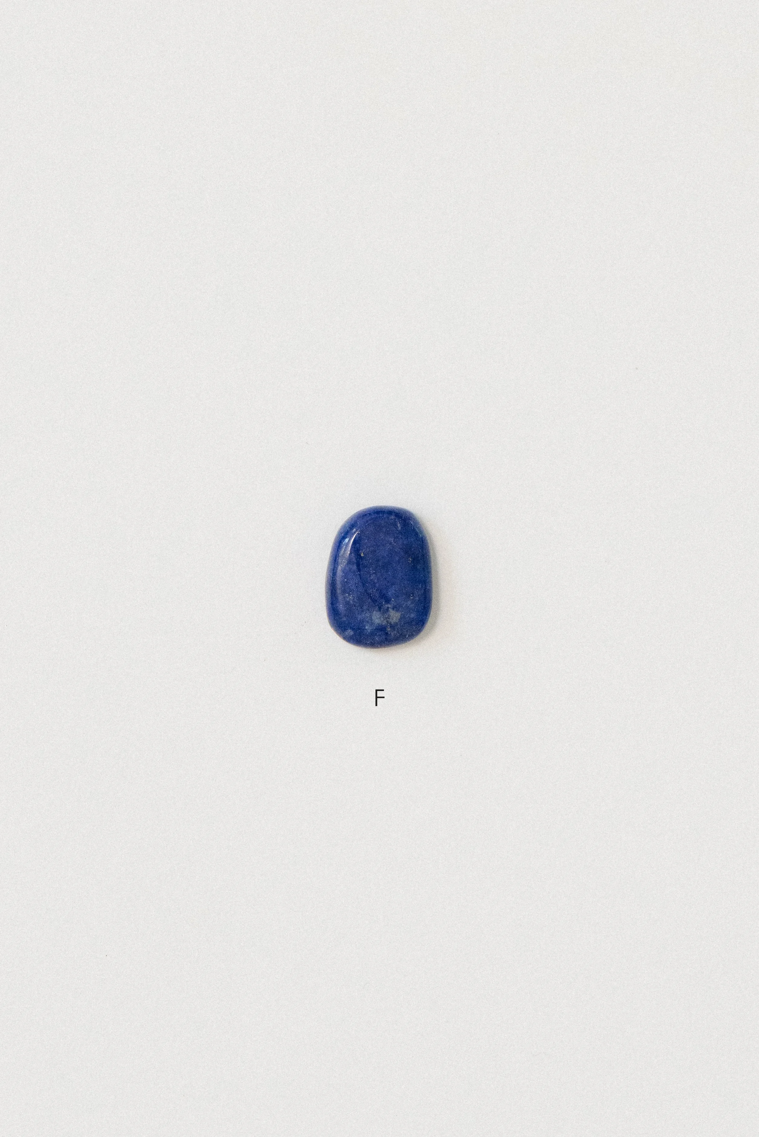 Single polished lapis lazuli stone from Afghanistan labeled 'F' on a white background, featuring a soft rectangular shape with a smooth surface and rich blue color.