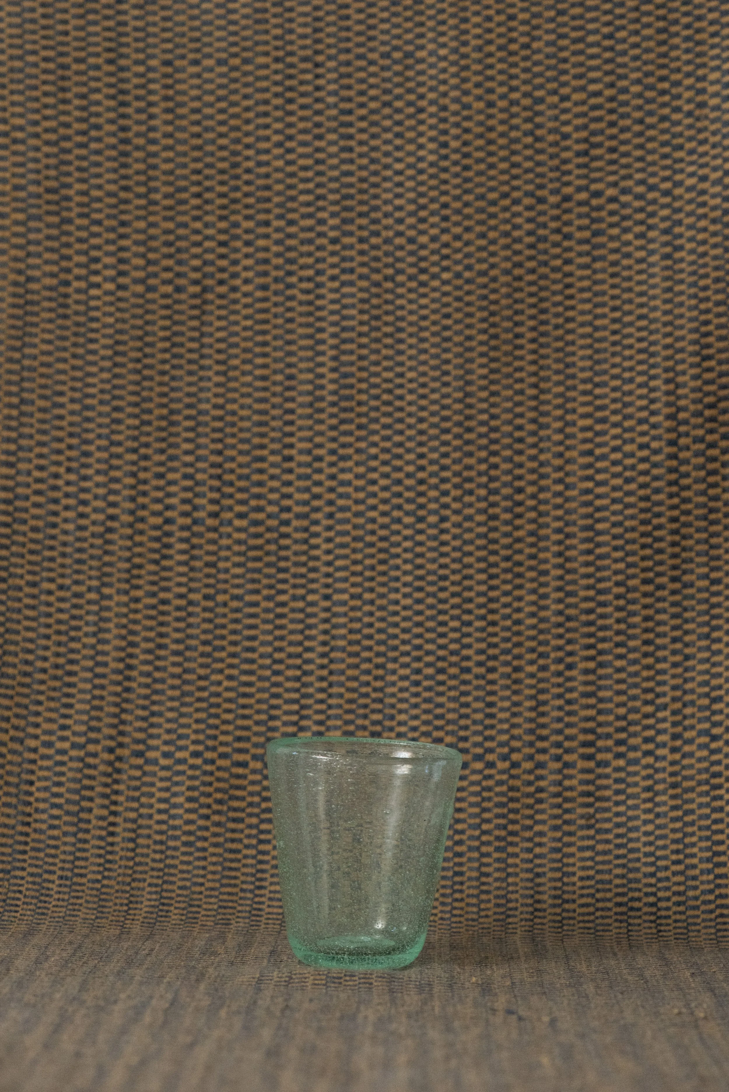 Handblown Egyptian seed glass cup in light green with delicate bubbles, displayed on a woven textile background.