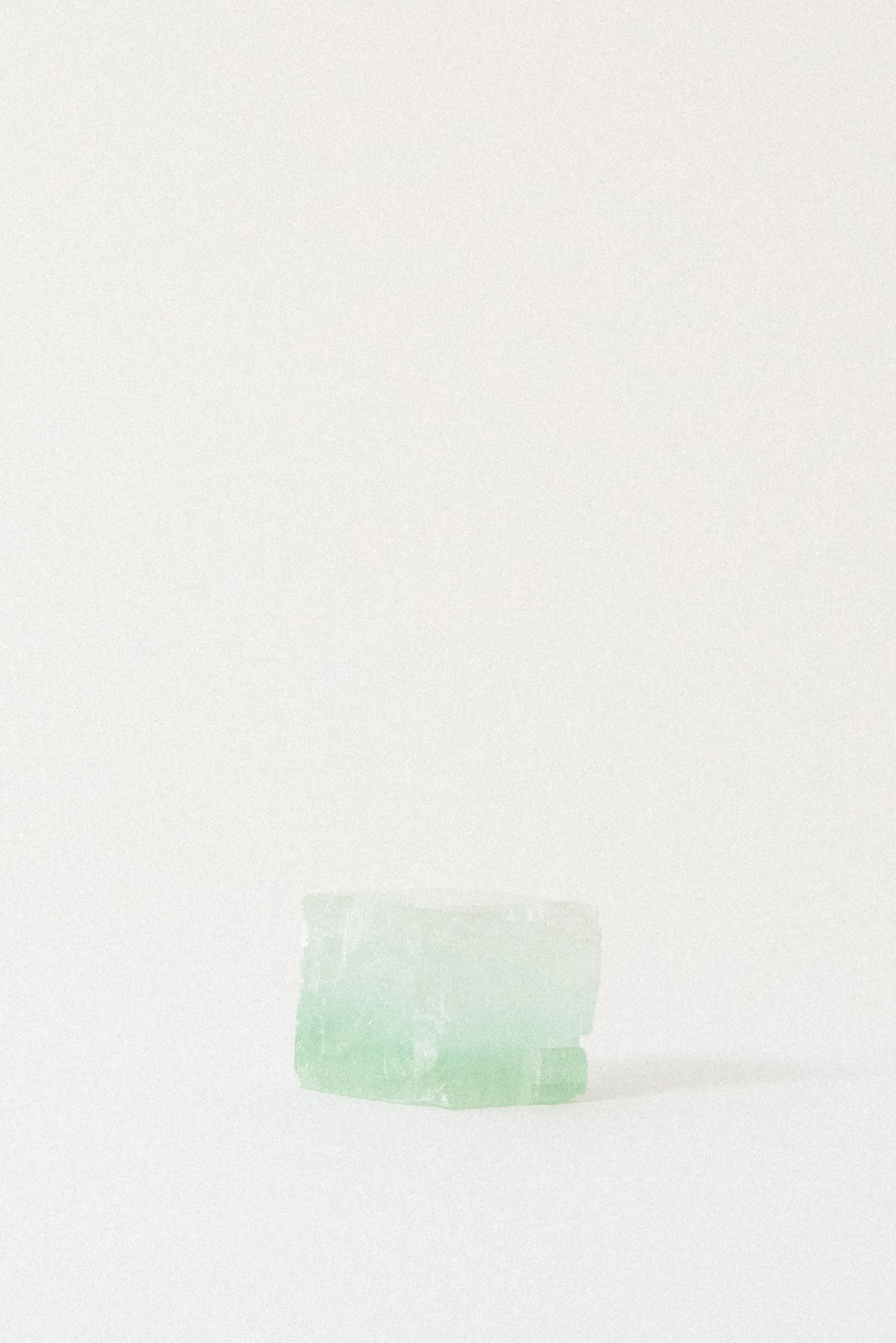 Green calcite rhomboid from Mexico lying flat on a white background, with soft mint and seafoam gradients and natural crystalline texture
