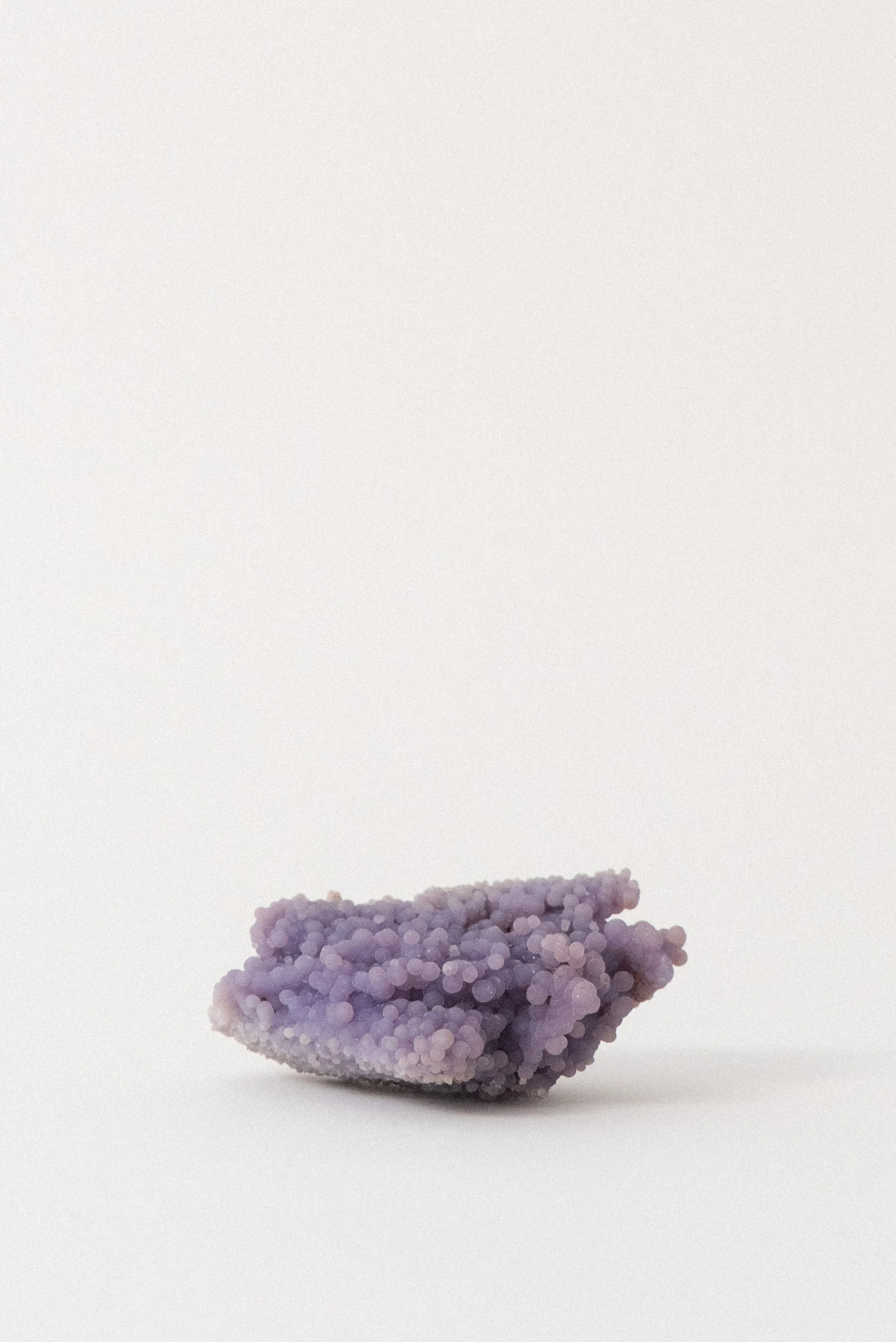 Flat, botryoidal purple grape agate crystal specimen with rounded formations from Sulawesi, Indonesia, displayed on a white background.