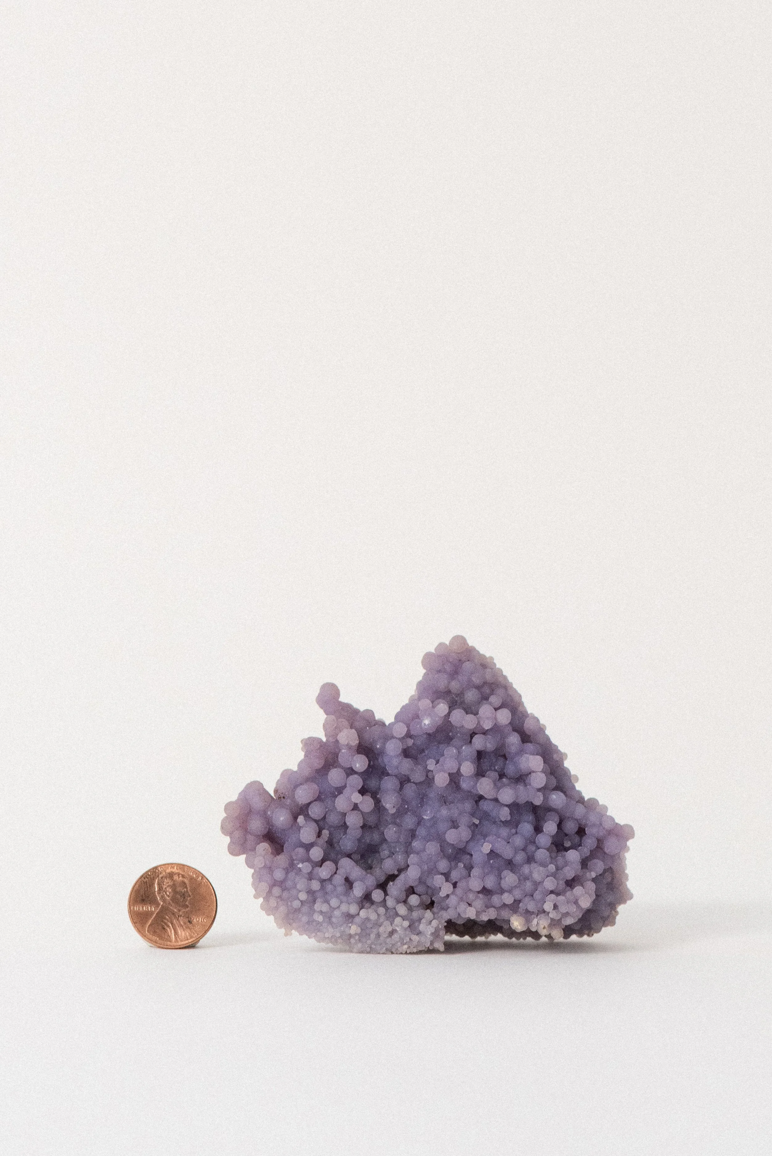 Purple grape agate mineral cluster from Sulawesi, Indonesia, shown next to a US penny for size reference on a white background.