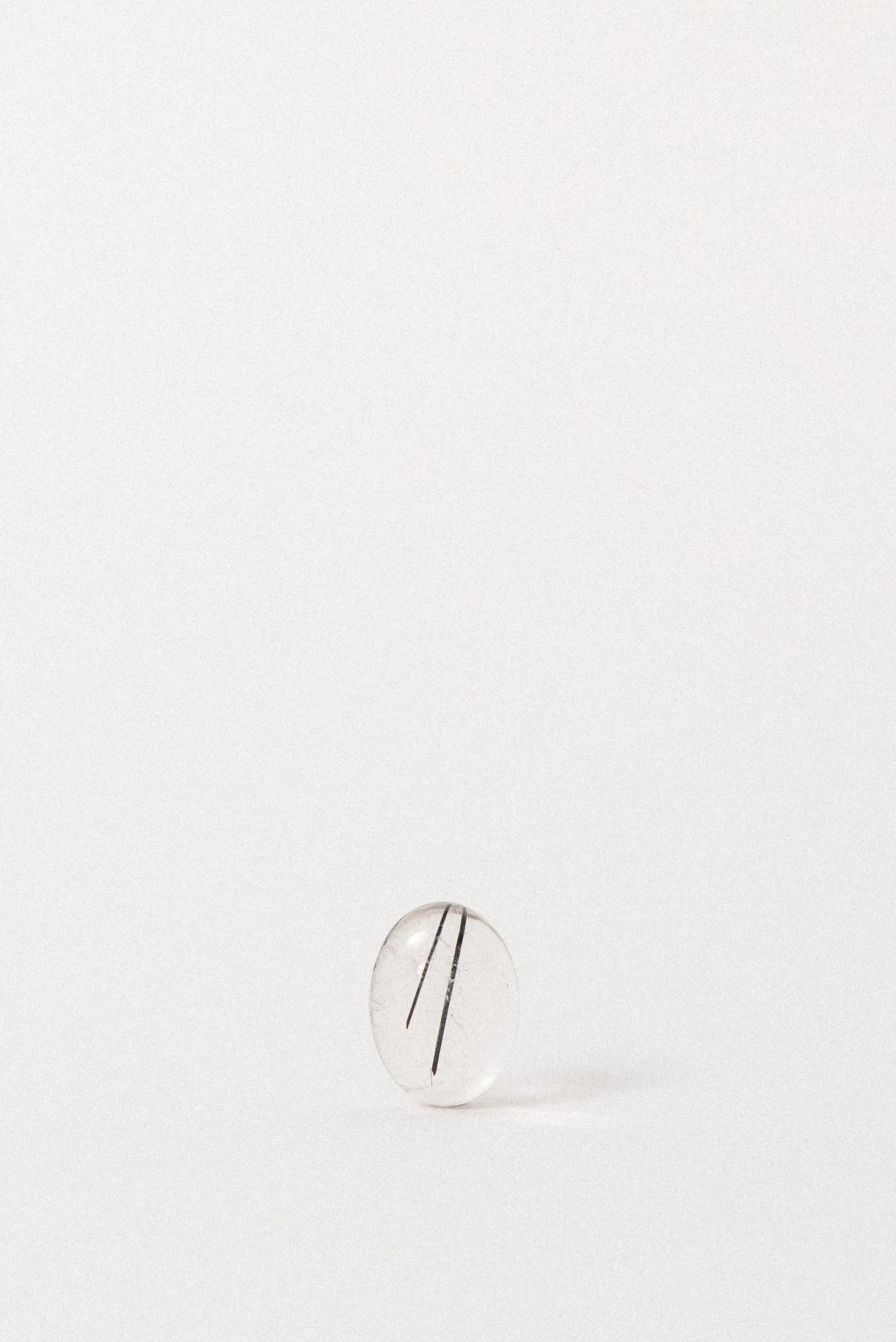 Clear quartz cabochon with black tourmaline inclusions from Brazil, shown upright.