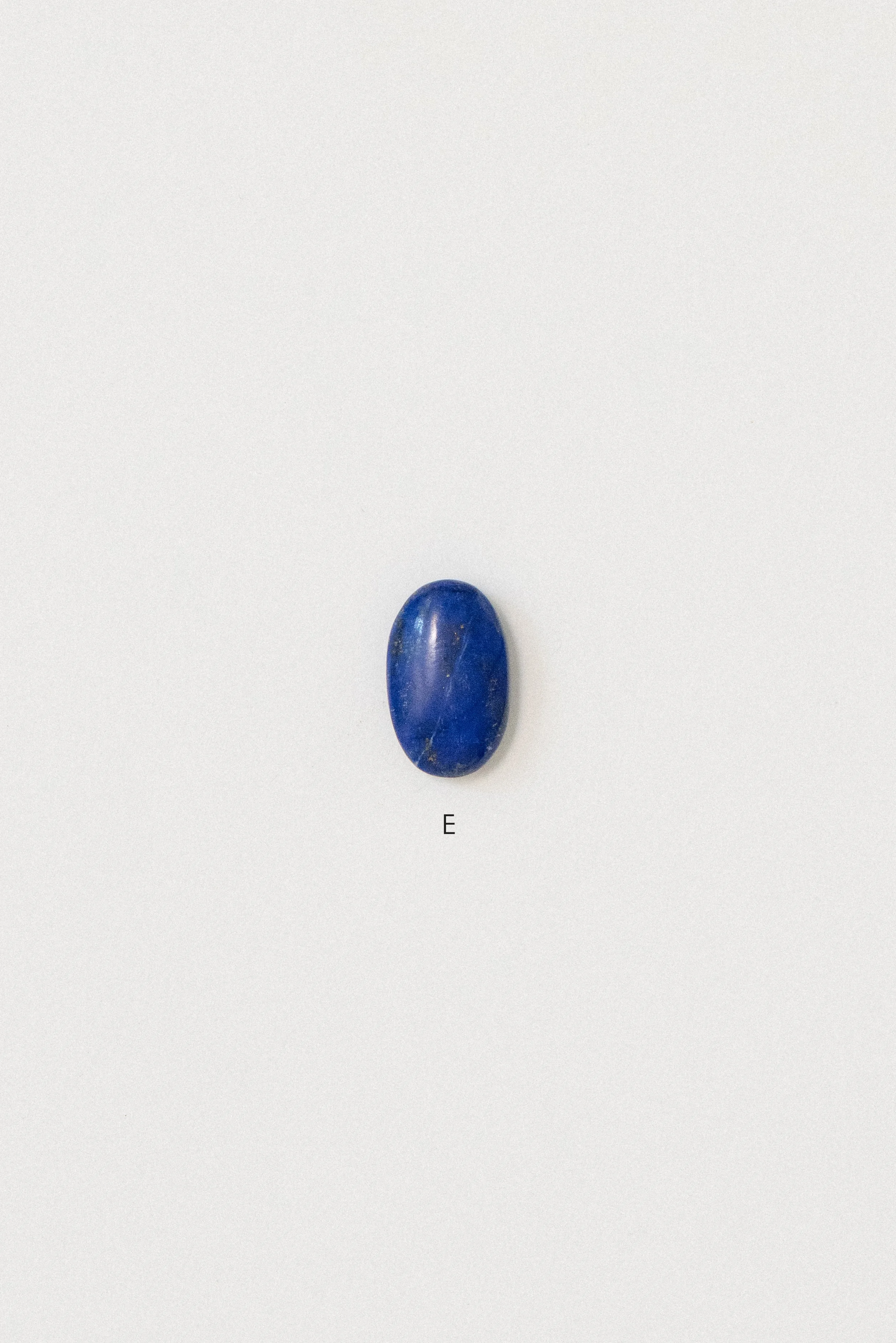 Single polished lapis lazuli stone from Afghanistan labeled 'E' on a white background, featuring an oval shape with minimal veining and deep blue color.