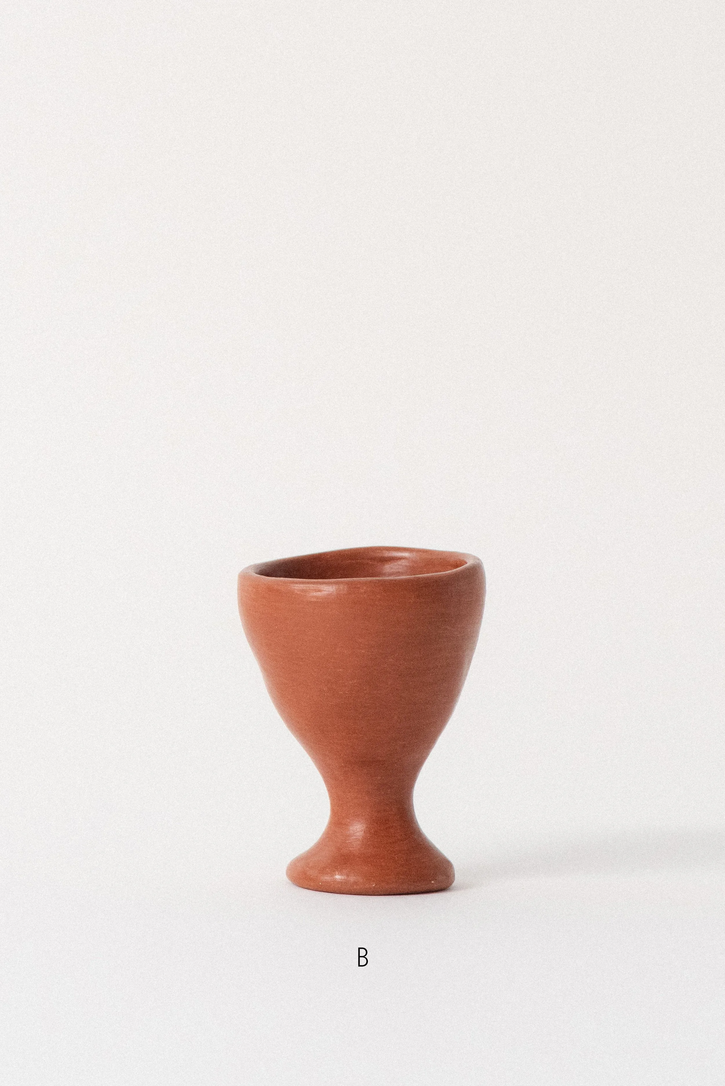 Single handmade barro rojo red clay egg cup labeled B, crafted in Oaxaca, Mexico, displayed against a white background — rustic and functional tableware.