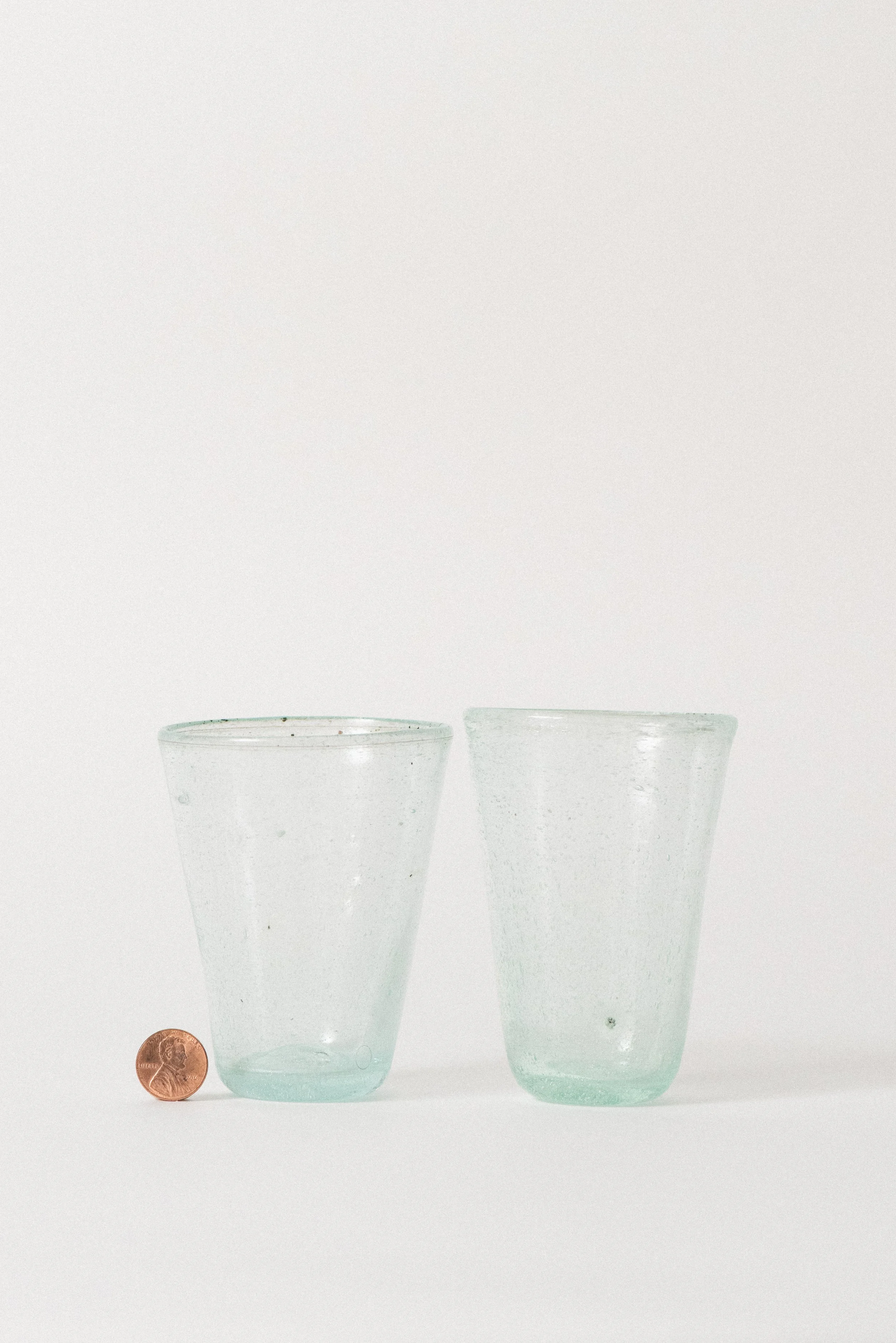Two handblown Egyptian seed glass cups shown next to a penny for scale, highlighting petite size and handmade texture.