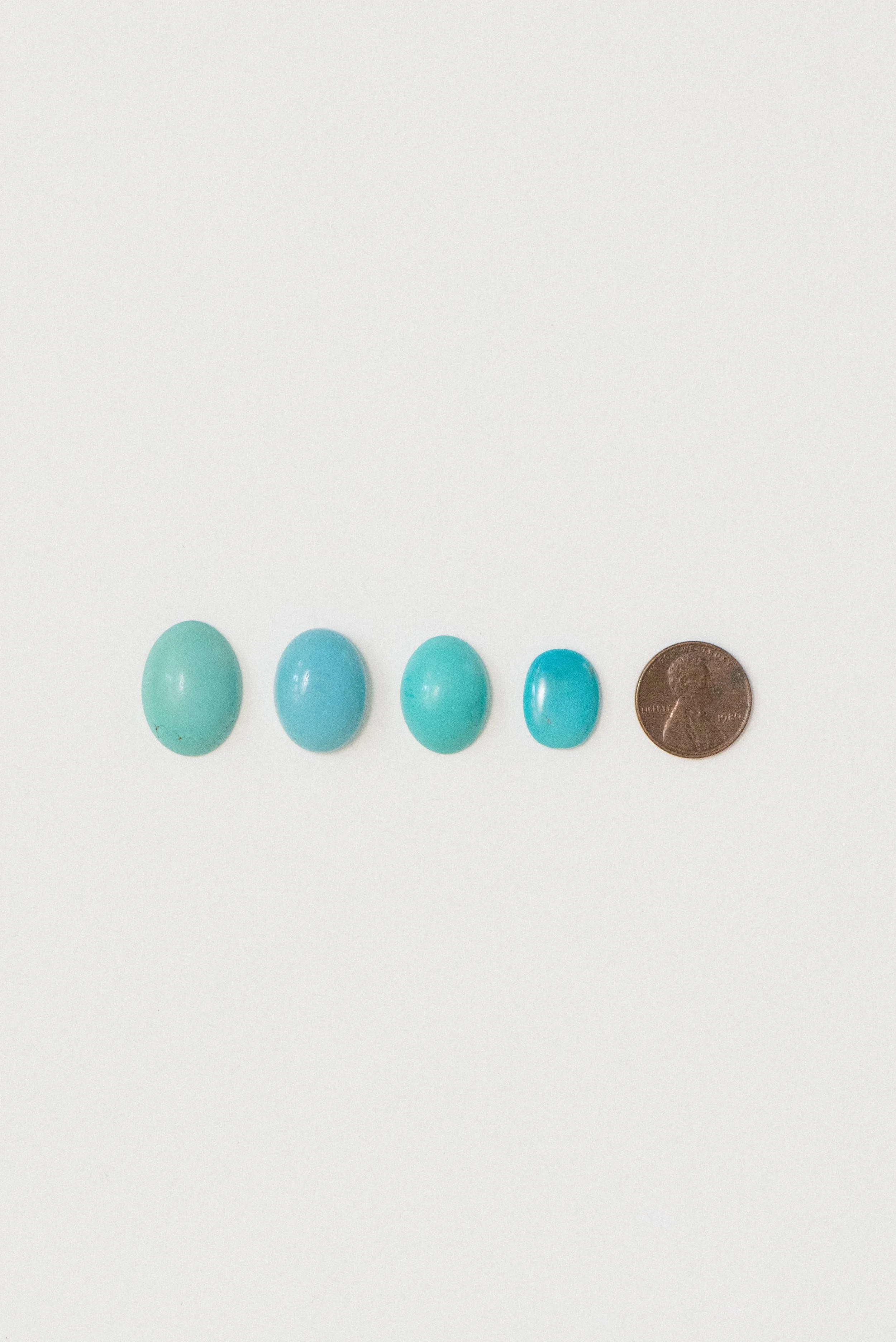 Natural turquoise cabochons from Sinai, Egypt in varying sizes, shown with a penny for scale on a white background.