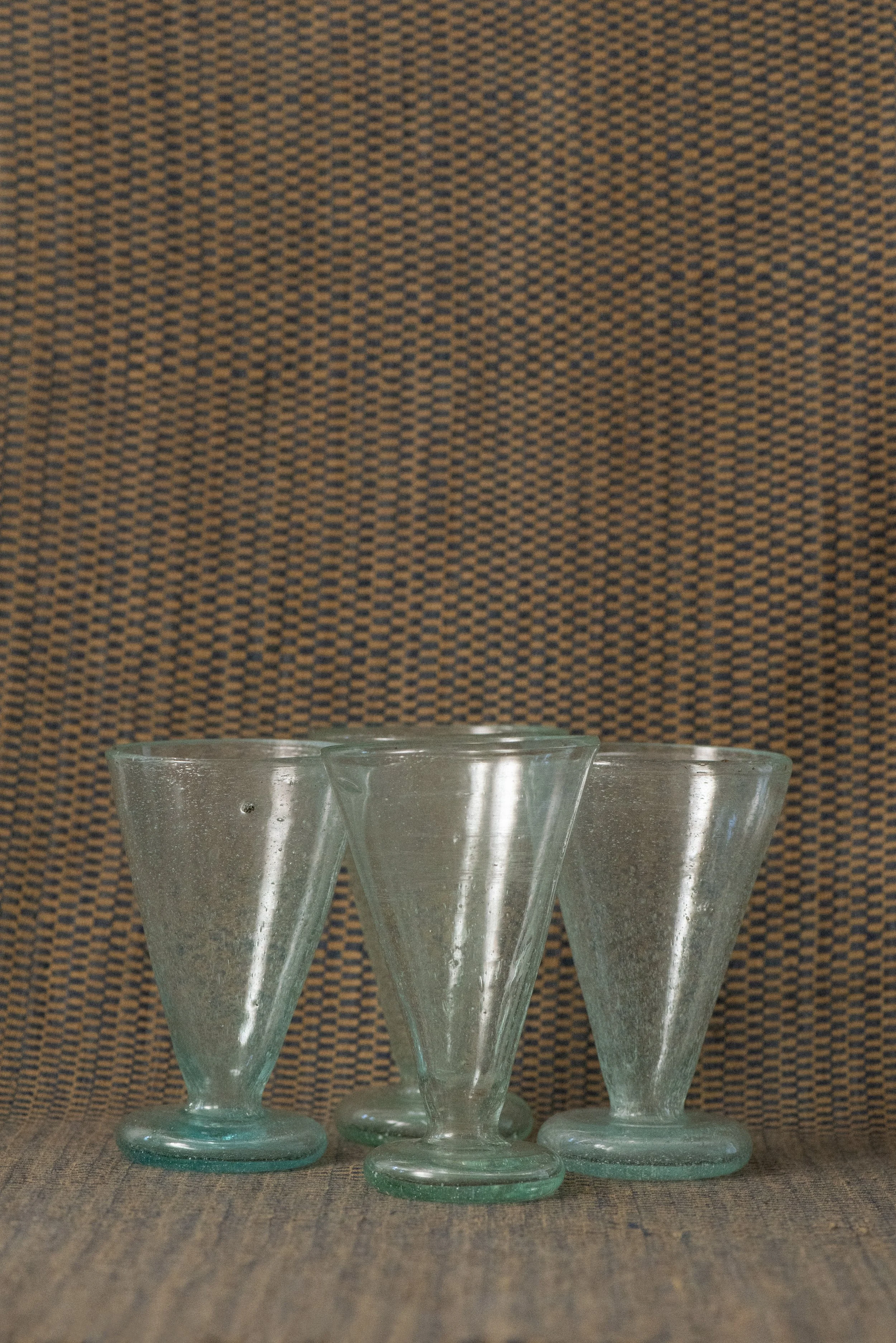 Handblown Egyptian seed glass footed cups in light green with natural bubbles, displayed on a woven textile background.