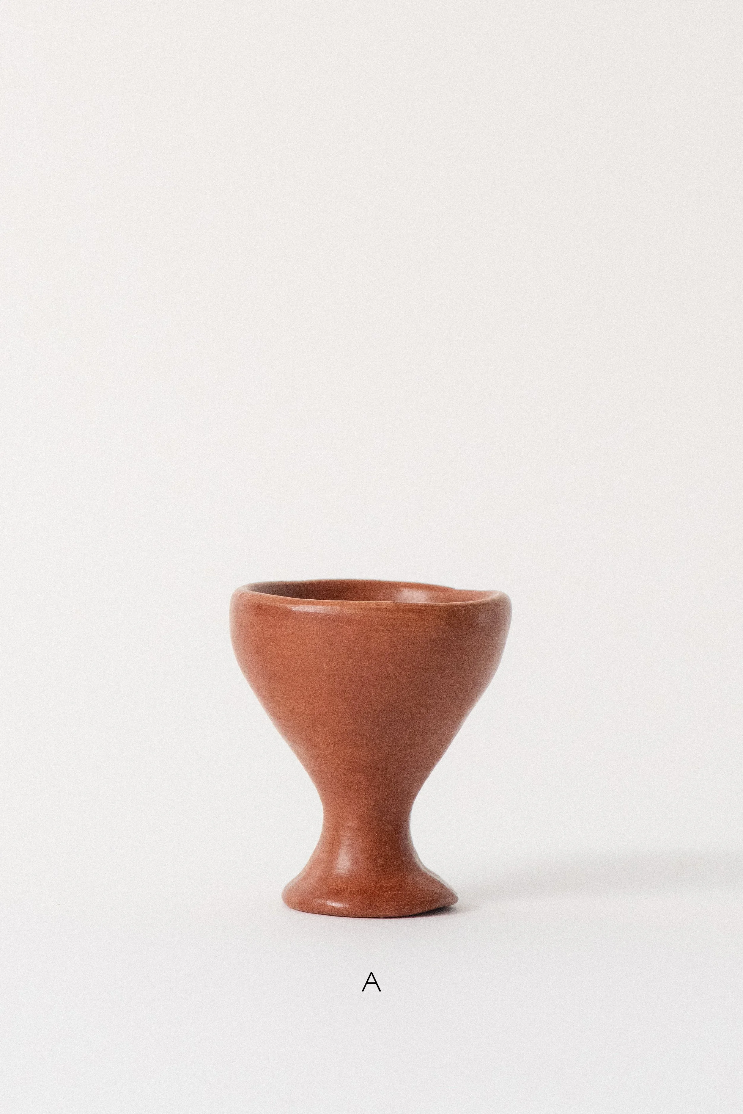 Single handmade barro rojo red clay egg cup labeled A, crafted in Oaxaca, Mexico, displayed against a white background — rustic and functional tableware.