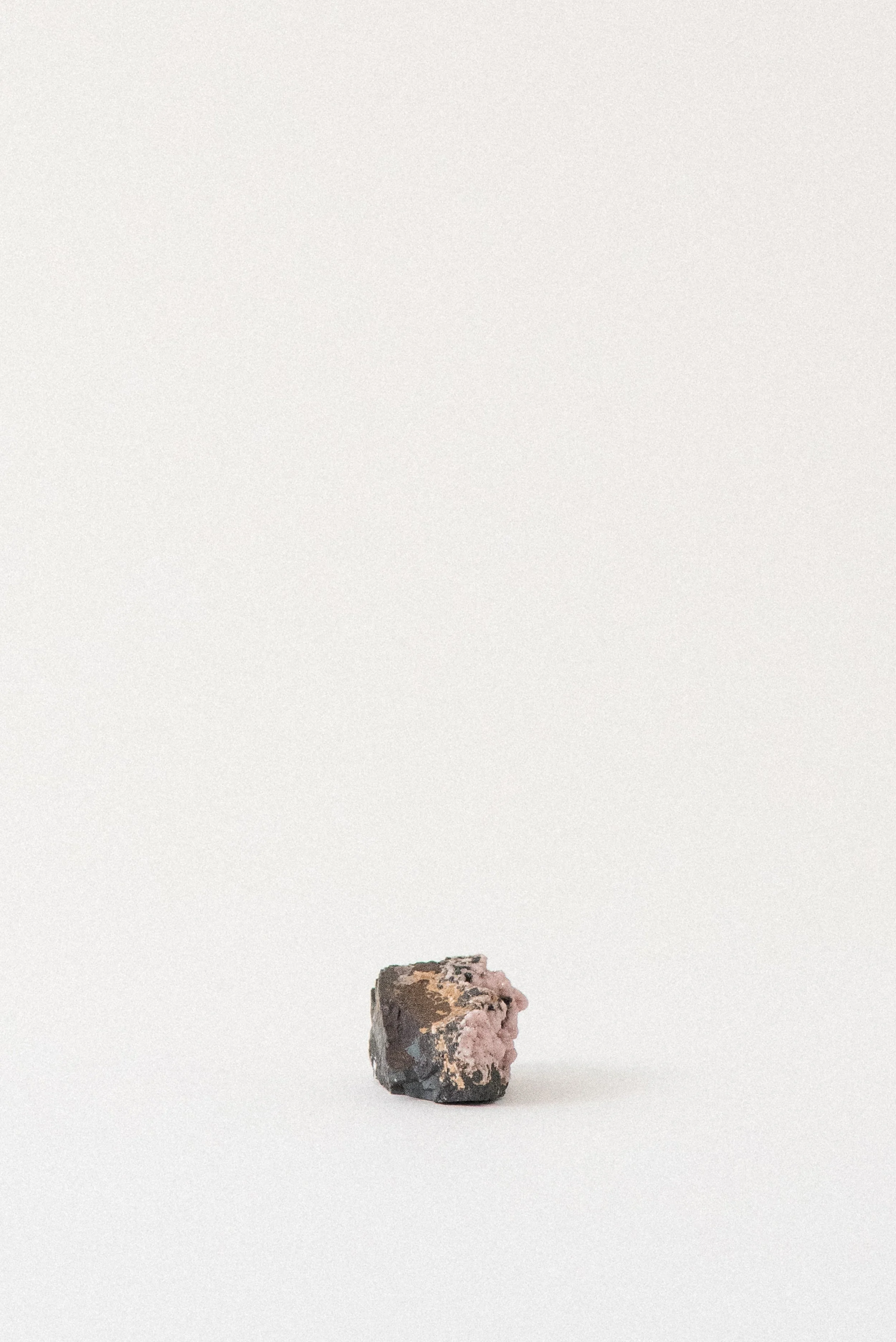 Small pink rhodochrosite crystal cluster on dark matrix from N’Chwaning Mine, South Africa, displayed on a white background.
