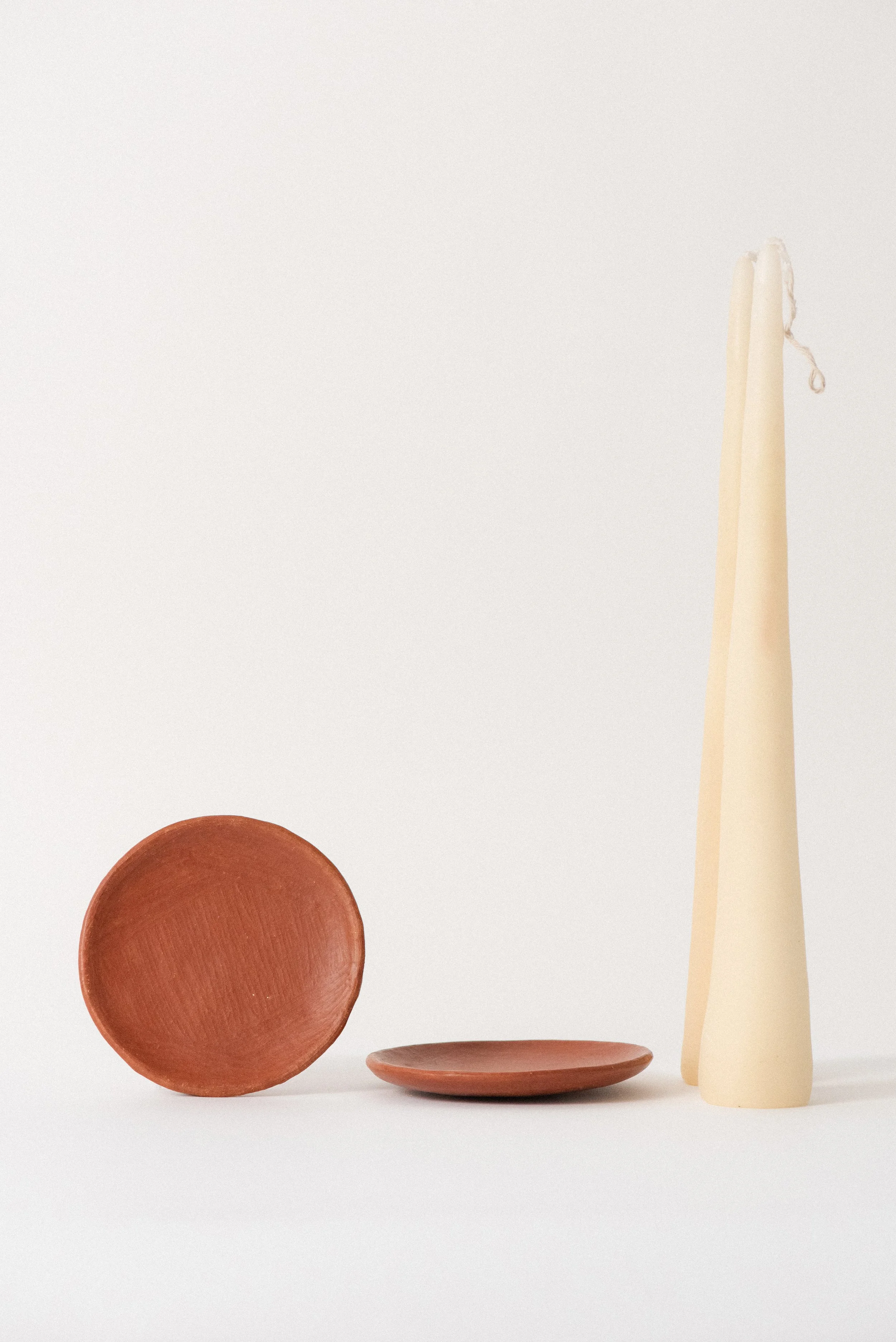 Close-up of handmade red clay barro rojo candle plates with Oaxaca beeswax taper candles beside them.