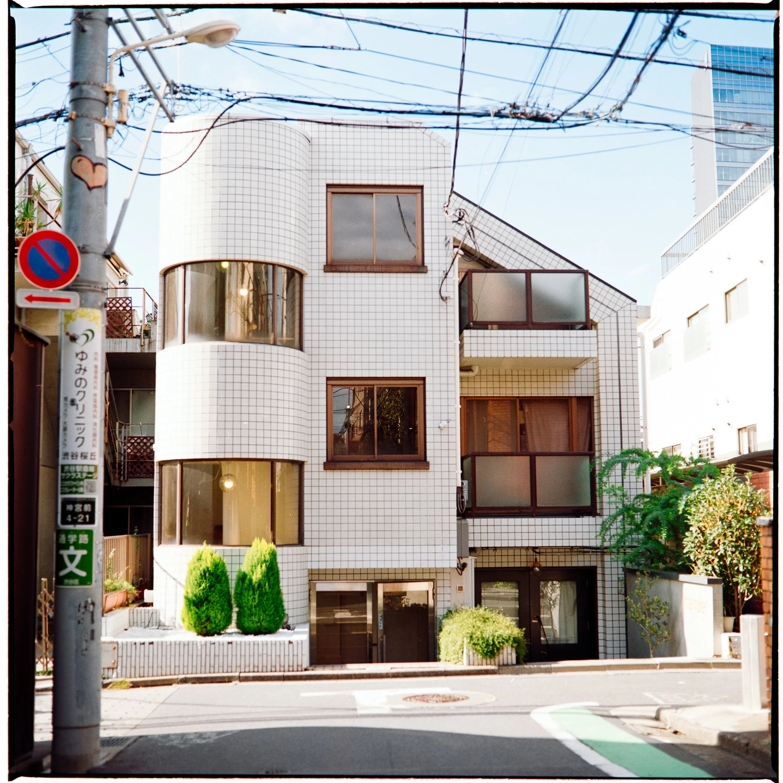 A white tiled home with striking geometry sits at the end of a street, lines crisscross everywhere connecting it to all the others.  Photographed on 120mm film in Tokyo, Japan.  Kodak Gold, home developed and scanned.