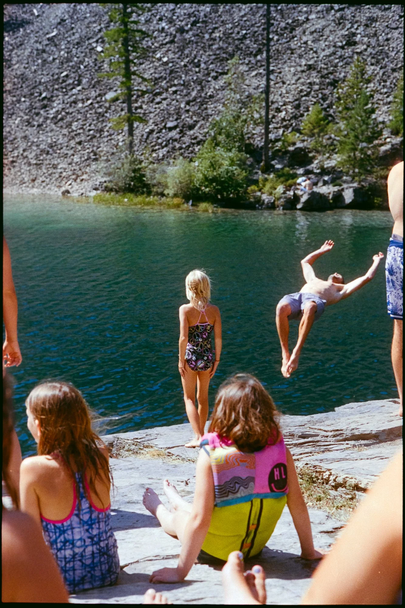 a man does a backflip off a cliff while a group of children watch.  Photographed on 35mm colour film, the image has a nostalgic and analog feeling.