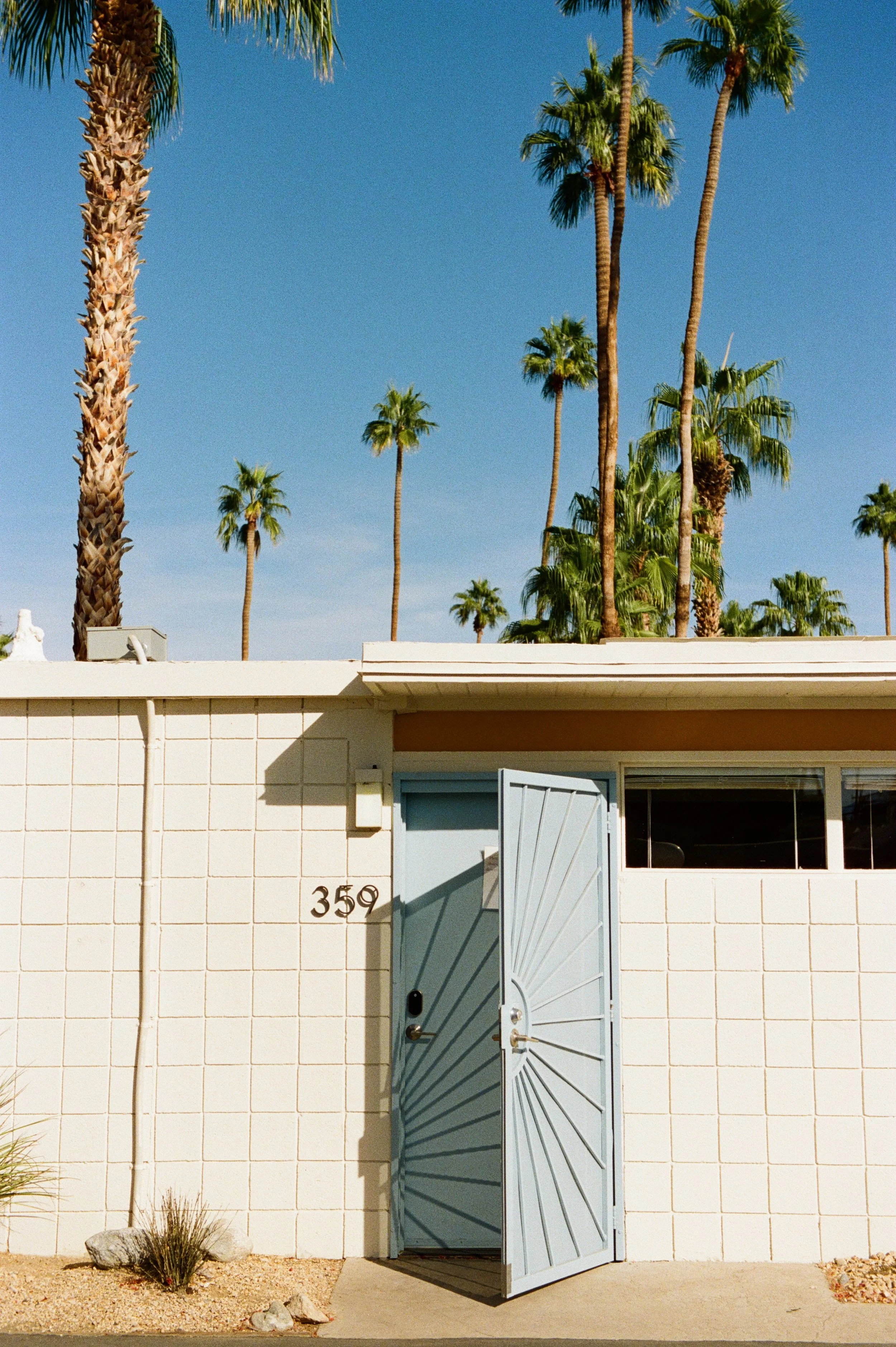 A door is partially opened creating the shadow of the sun on a mid-century modern apartment at Ocotillo Lodge in Palm Springs.  Photographed on 35mm with Kodak Gold.