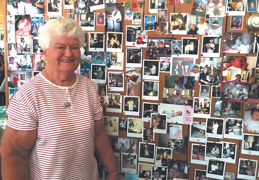 FOR THE KIDS : Dot Bottaro stands next to a wall of photos of youngsters her efforts as coordinator of the Children’s Thrift Shop at St. Peter’s Catholic Church in Liberty have helped. Bottaro has run the shop for 32 years. Emily Ball photo