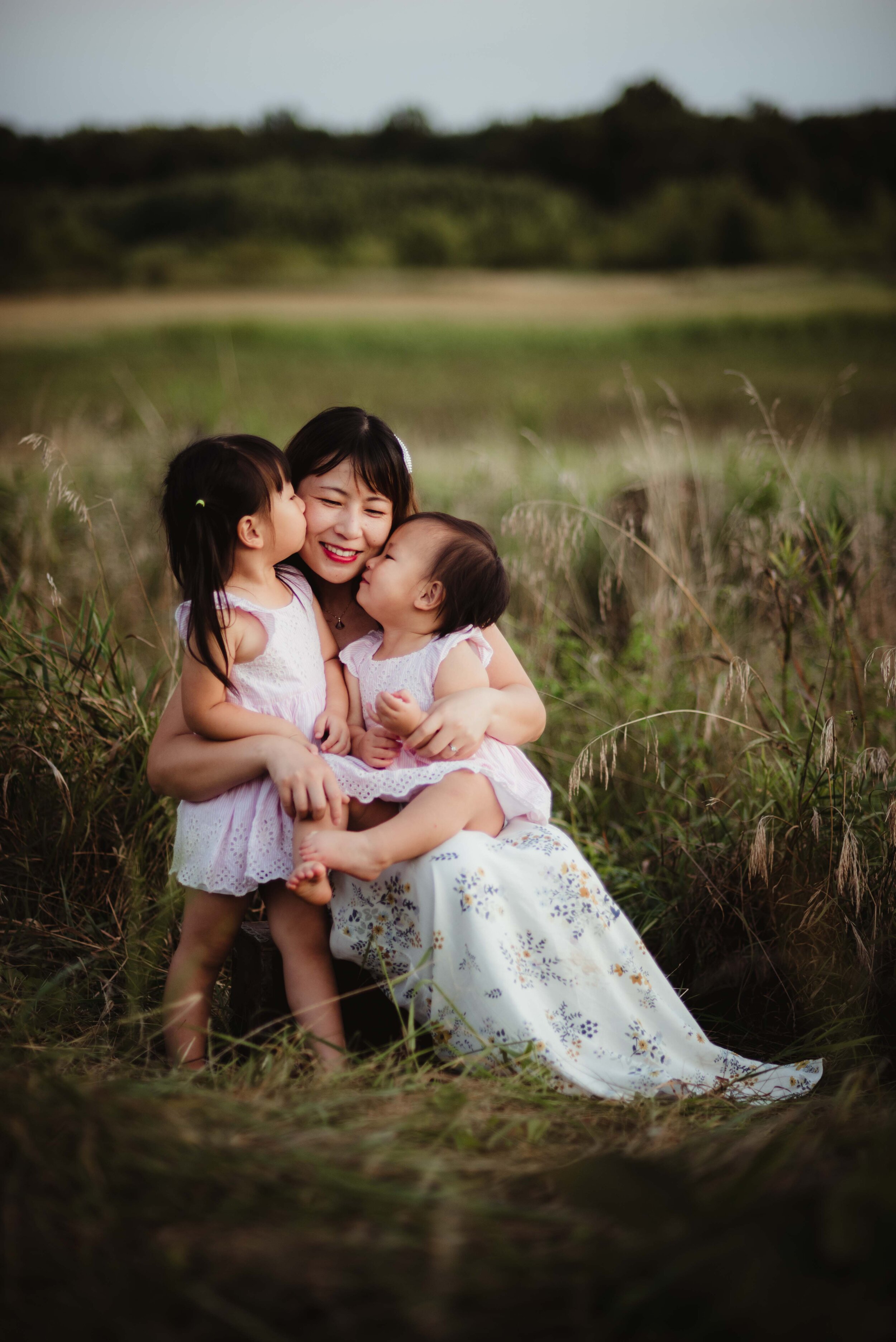 A mother has a sweet moment with her two little daughters in a summer field in West Lafayette, Indiana during their family photo session