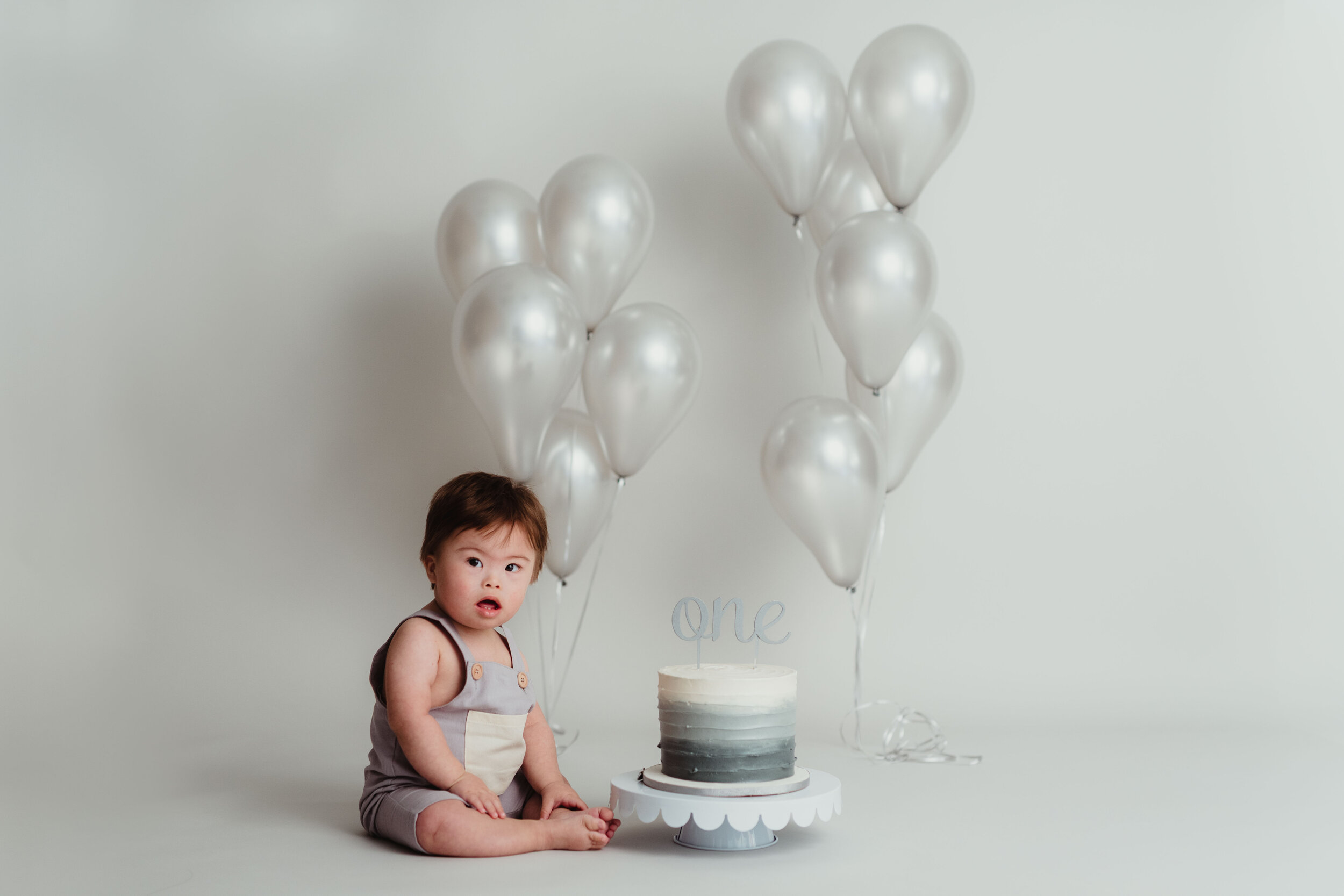 a first birthday cake smash with minimal gray and cream balloon design at Kelly McPhail Photography Studio in Lafayette, IN.