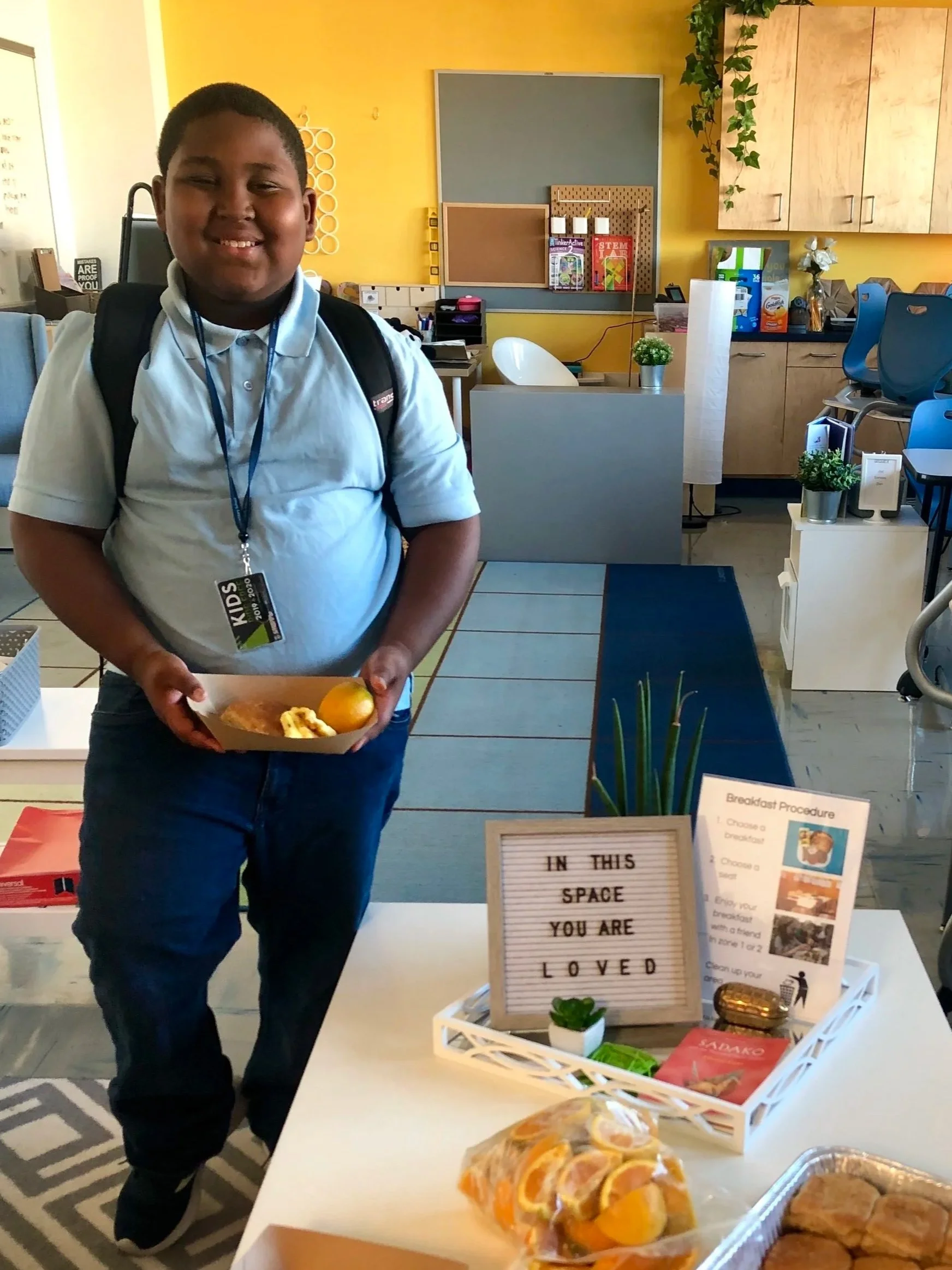 a 4th grade boy smiles next to a sign that says "in this space you are loved"