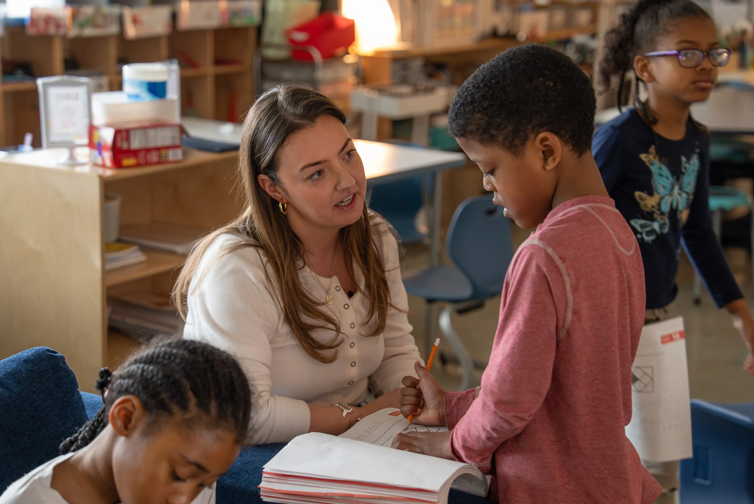 a female teacher sits at eye level with a 1st grade student, discussing his reading