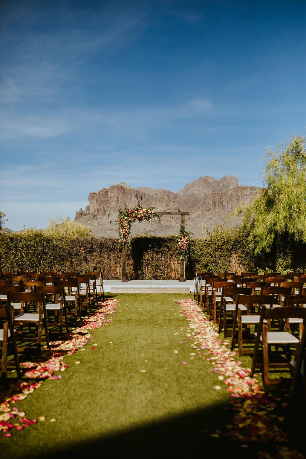 Wedding ceremony lawn with flower petals lining aisle and mountains in the background in Arizona